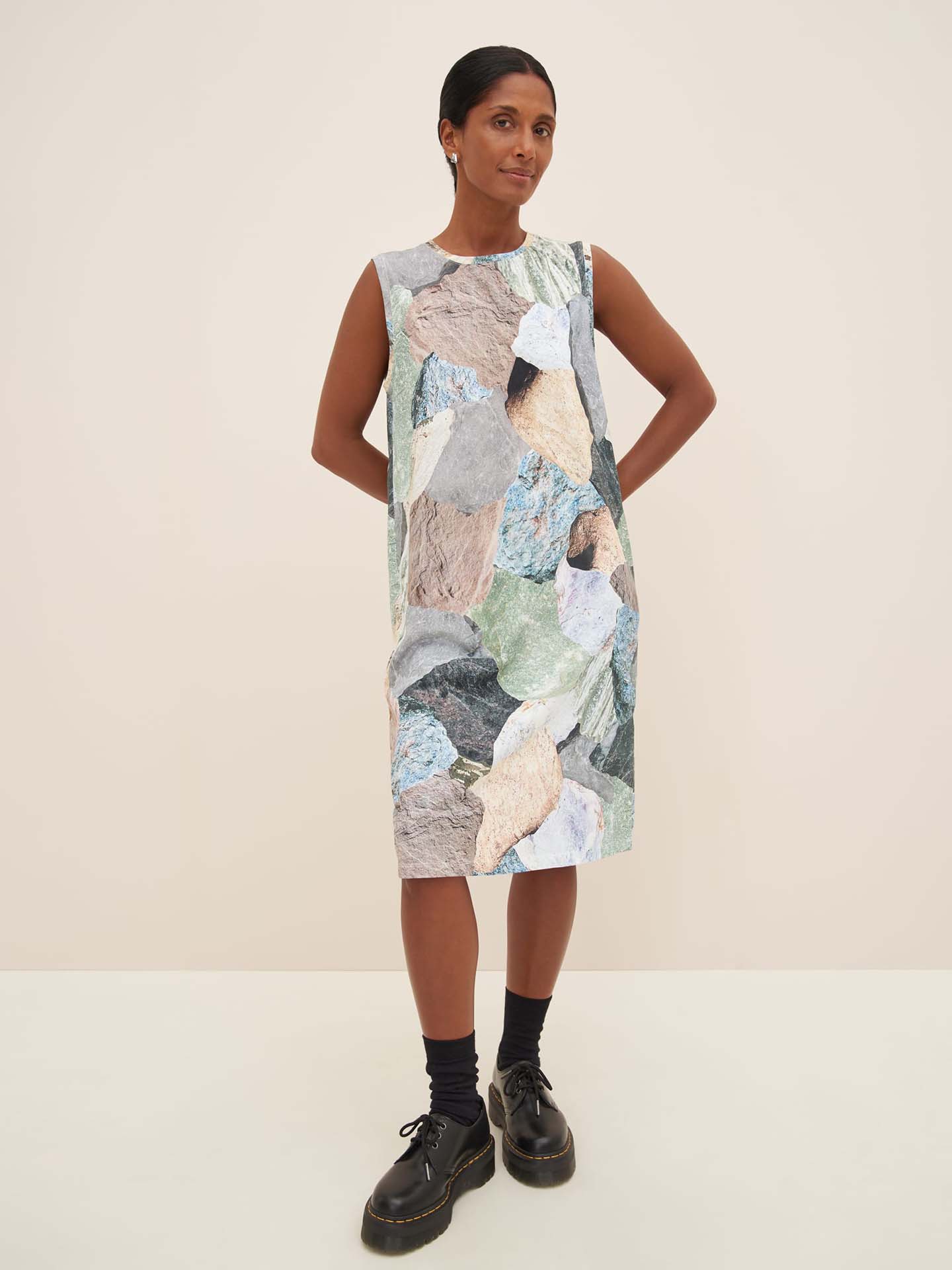 A person wearing the Mineral Singlet Dress by Kowtow, featuring a rock pattern and a close fit, poses against a plain background, complemented by black shoes and socks.