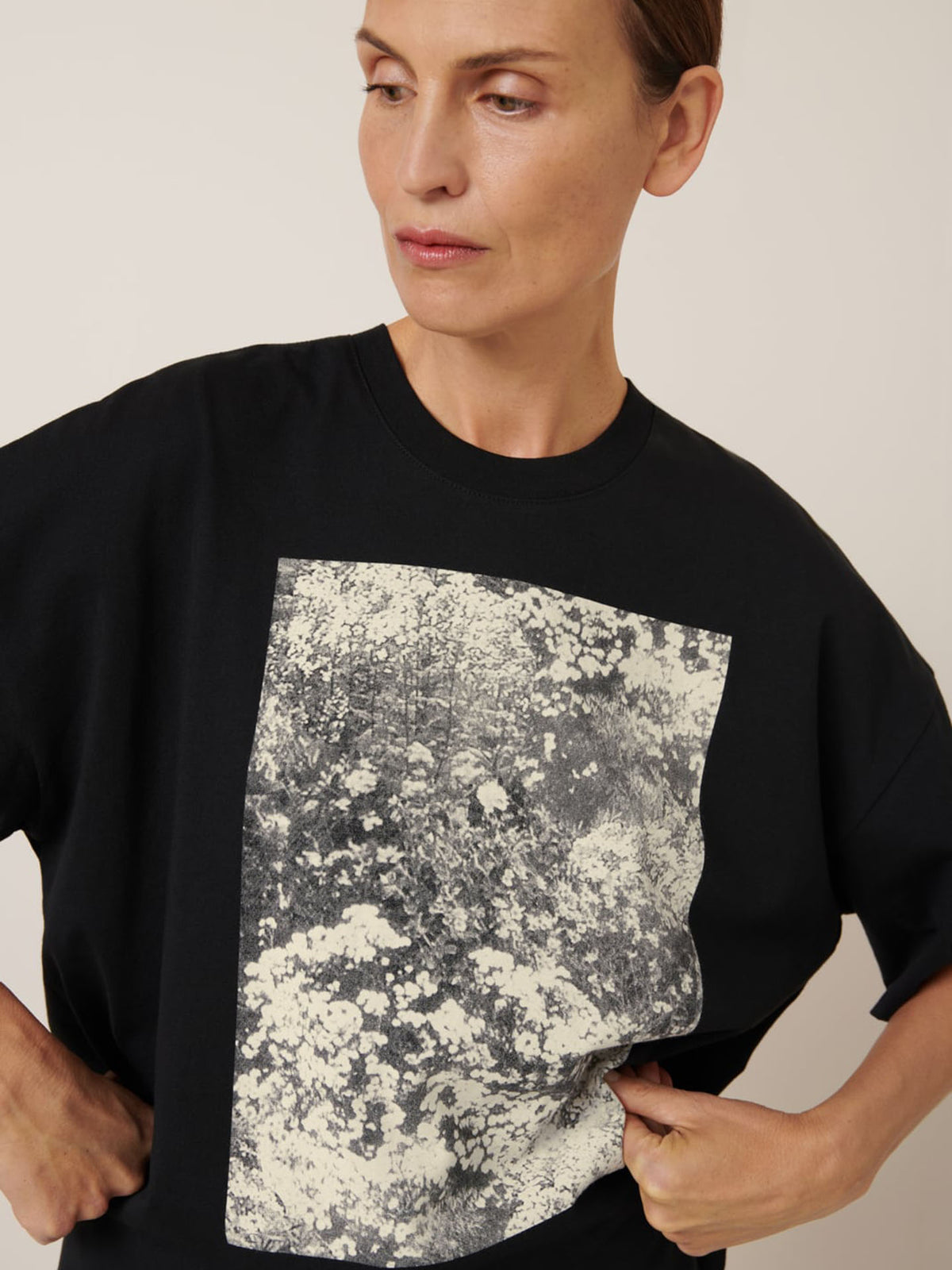 Wearing the Kowtow Monochrome Tee, the person stands against a plain background. The black T-shirt features a monochrome abstract pattern and an oversized fit for a relaxed, stylish silhouette, perfect for any casual outing.