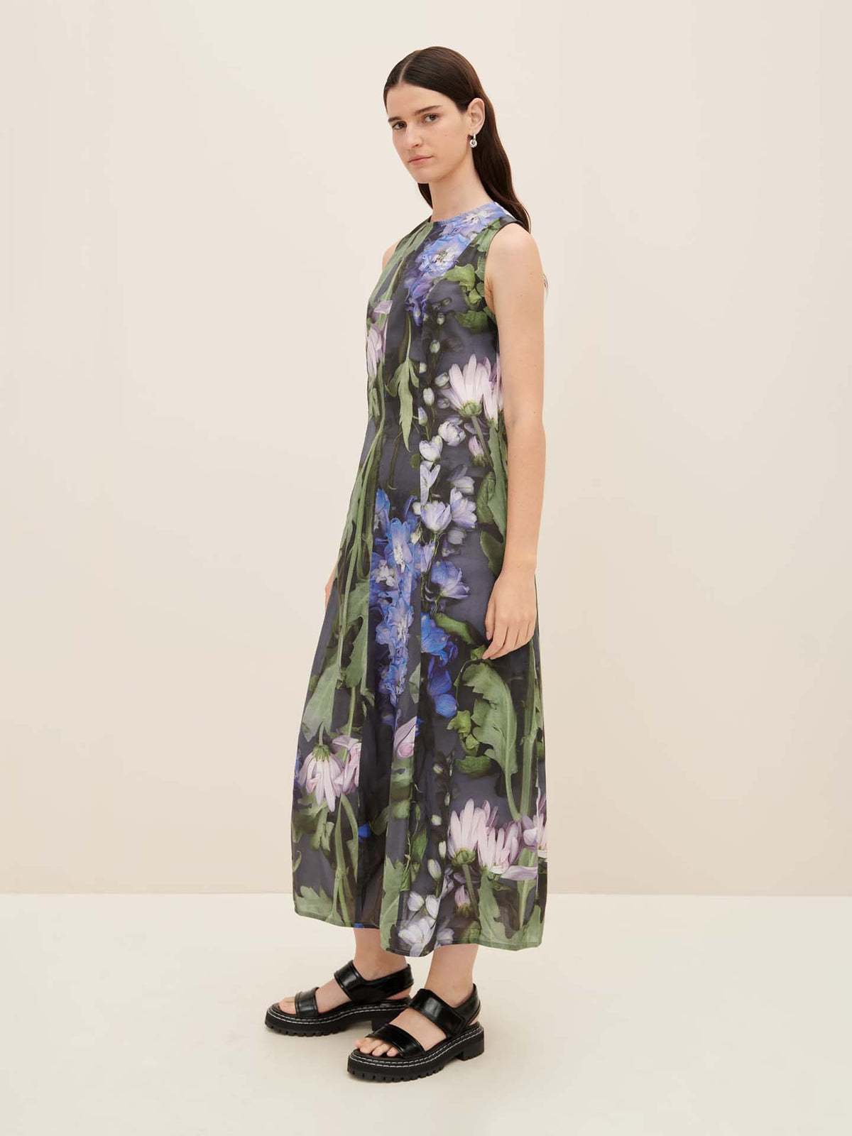 A person wearing the Mosaic Dress, a floral oversized sleeveless piece from Kowtow, paired with black sandals and posing against a plain background.