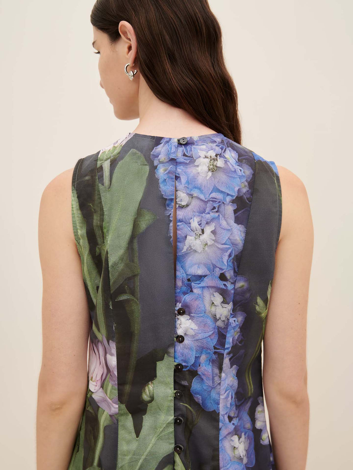 A person with long hair is modeling the Mosaic Dress by Kowtow, showcasing its oversized fit and floral pattern in blue and green hues, as seen from the back.