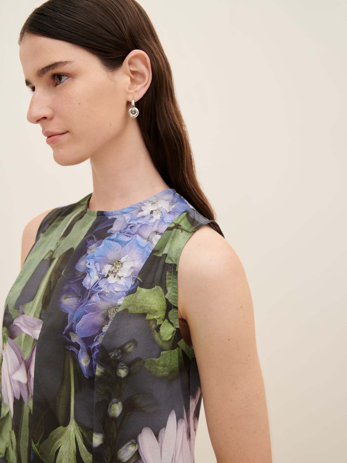 A woman with long dark hair is wearing the oversized sleeveless Kowtow Mosaic Dress, paired with round earrings, as she gazes to the side against a plain background.