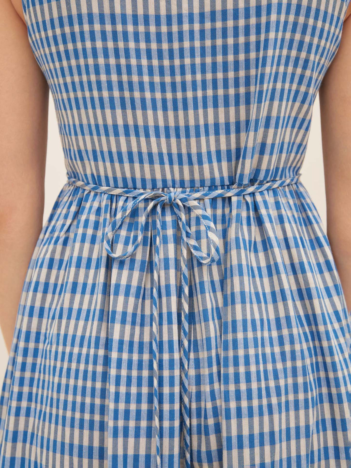 A close-up of the Outline Dress by Kowtow in size S, featuring a blue and white checkered pattern with a waist tie, viewed from the back. This dress ensures both style and comfort with its standard fit.