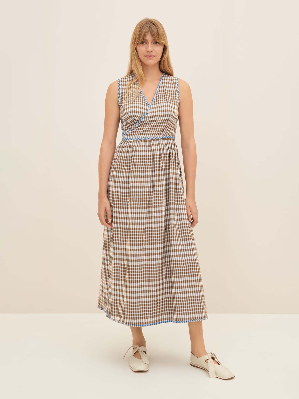 A person wearing the Outline Dress by Kowtow, featuring a sleeveless checkered design and standard fit, is paired with white shoes against a plain background. The ensemble exudes simplicity and elegance. For similar styles, consider consulting the size guide for Kowtow size S.