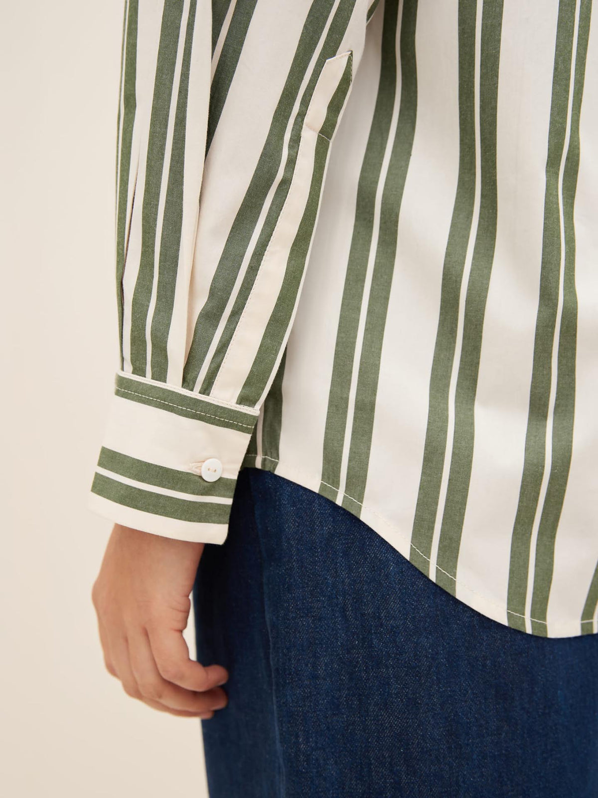 Close-up of a person wearing the Petra Shirt – Forest Stripe by Kowtow, styled with blue jeans. The white shirt features dark green vertical stripes and demonstrates an oversized fit. The focus is on the arm and part of the torso, providing an ideal reference for comparing with Kelsey measurements in our size guide.