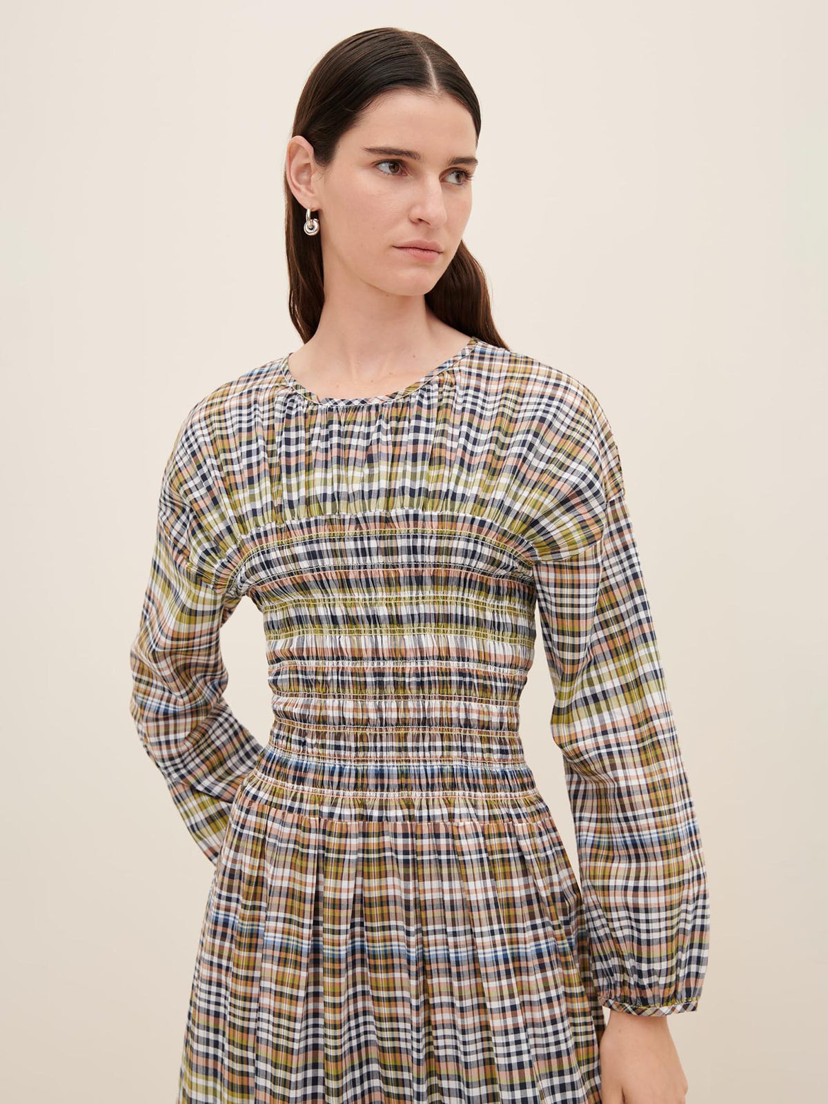 A person wearing Kowtow&#39;s Sienna Dress, featuring a long-sleeved, plaid pattern in a standard fit, looks to the side against a plain background.