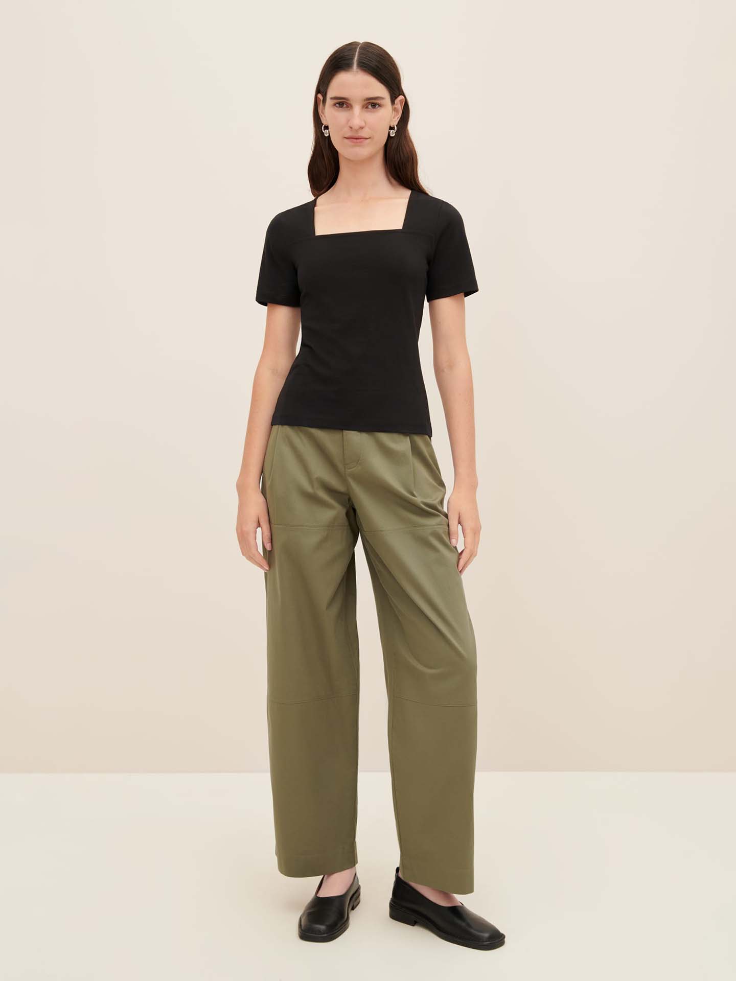 A woman in a Kowtow Square Neck Tee and oversized olive green wide-leg pants, paired with black shoes, stands against a plain light background. Be sure to consult the Kowtow size guide to find your perfect fit.