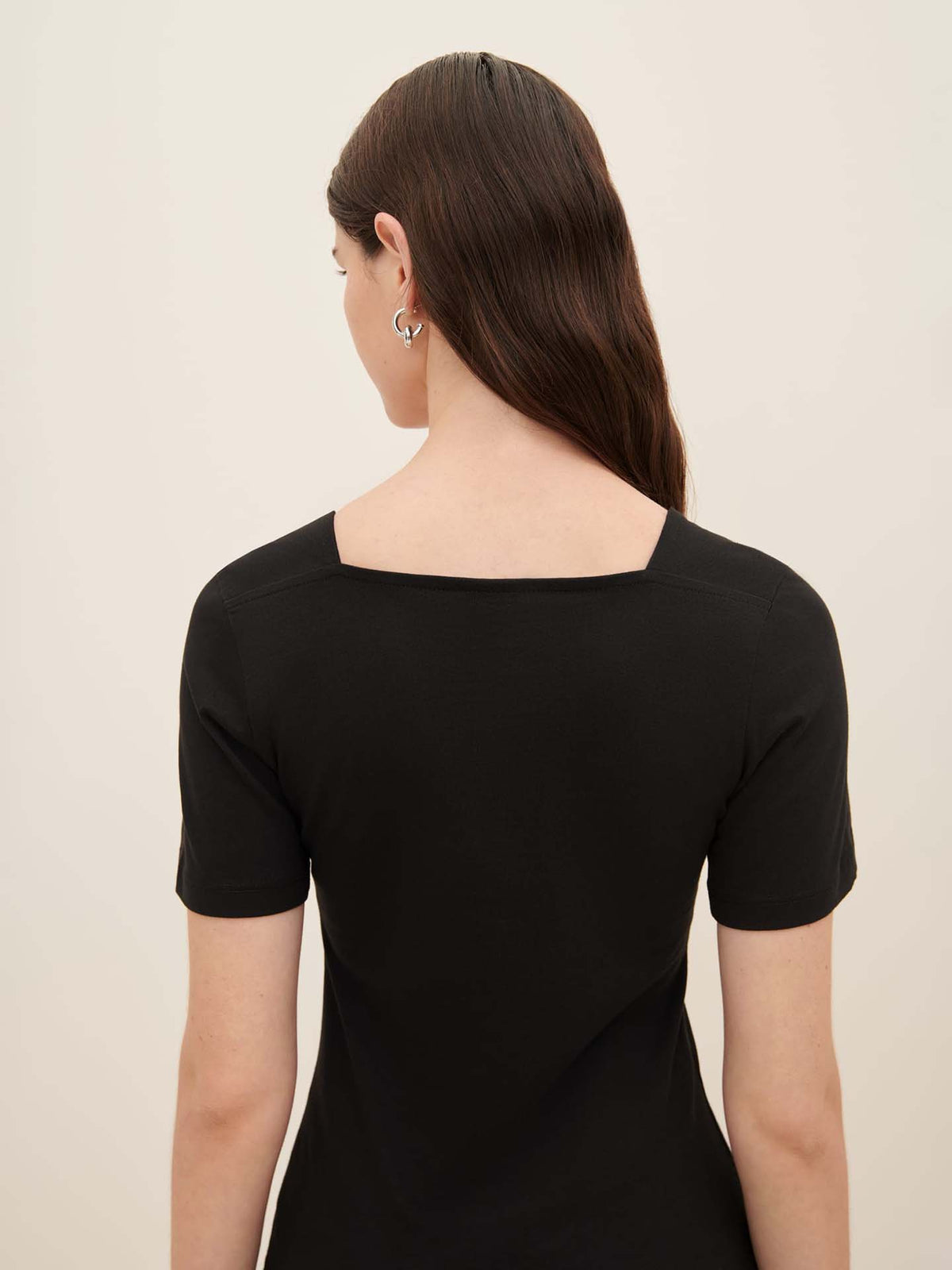 A person with long brown hair is seen from the back wearing an oversized black Square Neck Tee by Kowtow.