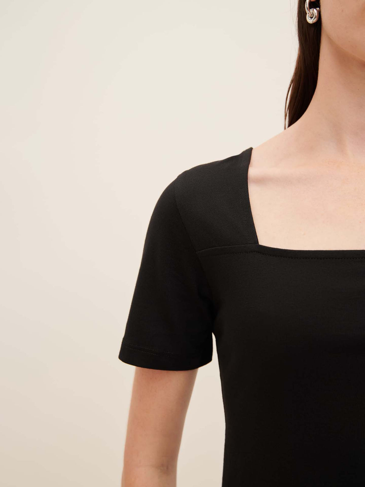 A model is wearing the Kowtow Square Neck Tee, which features a black color and an oversized fit, shown from shoulder to mid-torso against a plain background. For perfect fit recommendations, please refer to the Kowtow size guide.