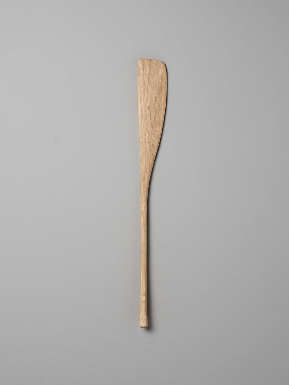 A Bakers Tool by Luke Crouch, hand-carved from Australian She-Oak with a flat, slightly curved end, is lying on a light grey background.