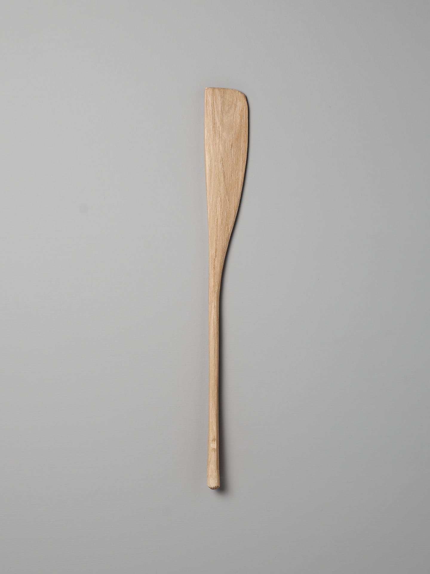 A Bakers Tool by Luke Crouch, hand-carved from Australian She-Oak with a flat, slightly curved end, is lying on a light grey background.