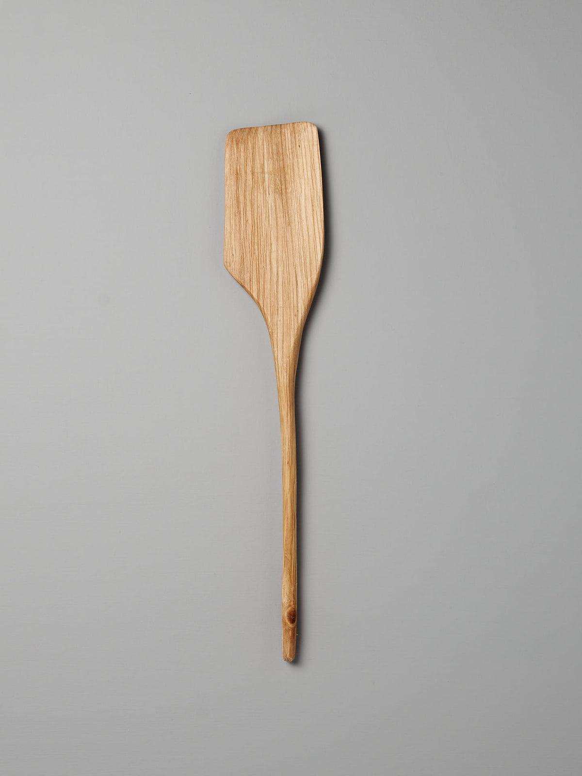 A Luke Crouch hand-carved Spatula, crafted from Australian She-Oak wood, featuring a flat, rectangular head and a long handle, lies on a plain gray background.