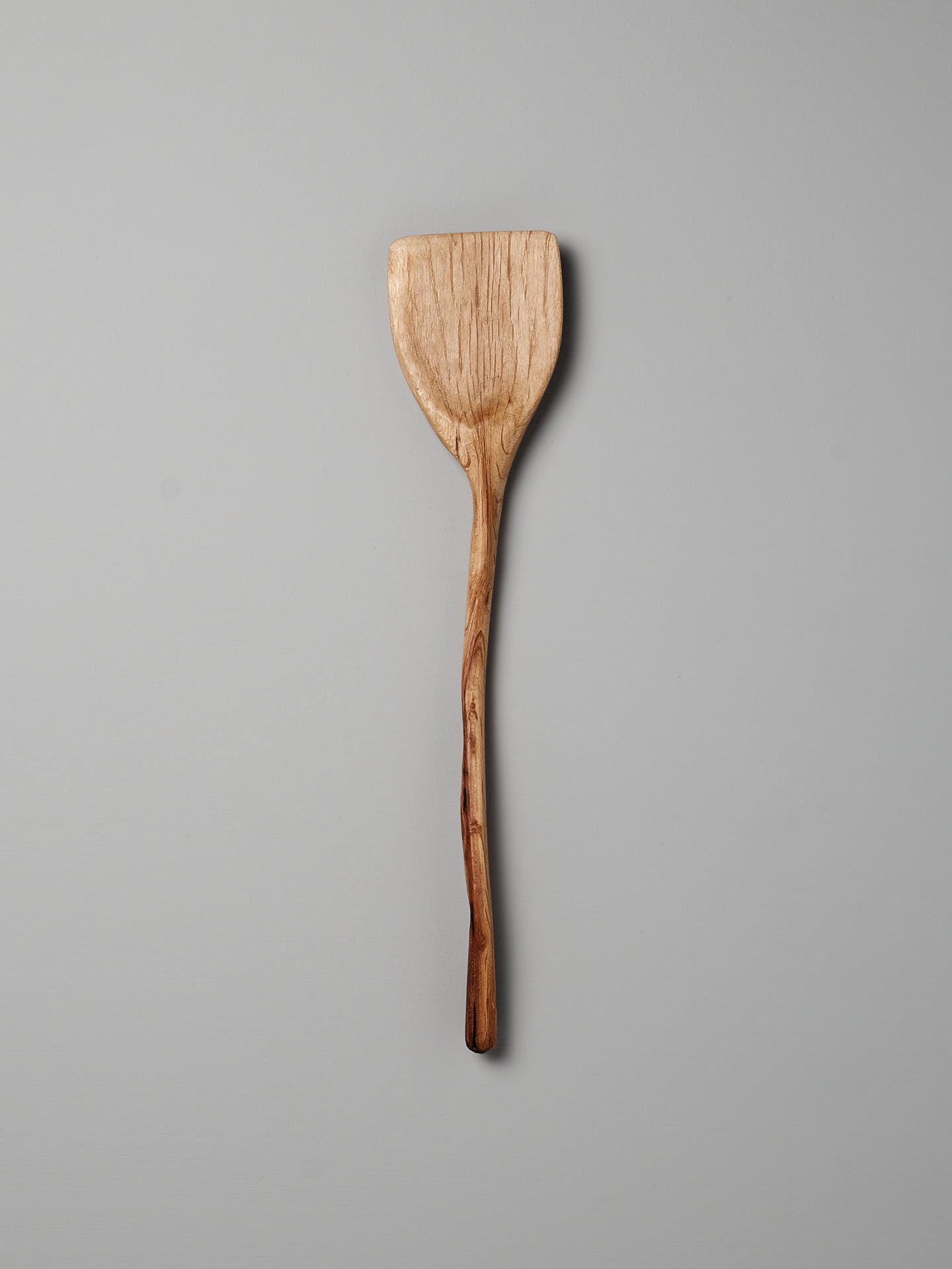 The Wok Tool by Luke Crouch is a hand-carved, wooden spatula featuring a flat, rectangular head and a smooth handle, made from Australian She-Oak using traditional techniques, set against a plain gray background.