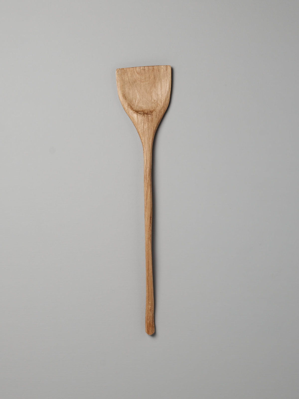 Wok Tool by Luke Crouch, featuring a flat, rectangular head and a long handle, hand-carved from Australian She-Oak, lying on a plain gray background.