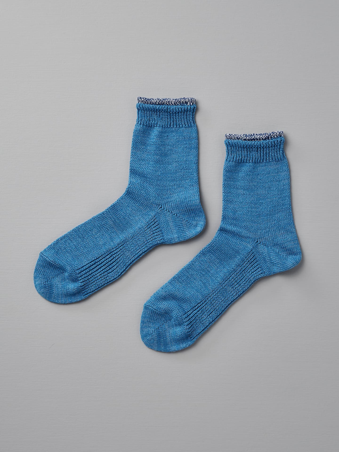 A pair of Mauna Kea Organic Top Switching Socks – Blue, sized EUR 35—38, are displayed on a white surface. They feature ribbed cuffs with a small, decorative white trim.