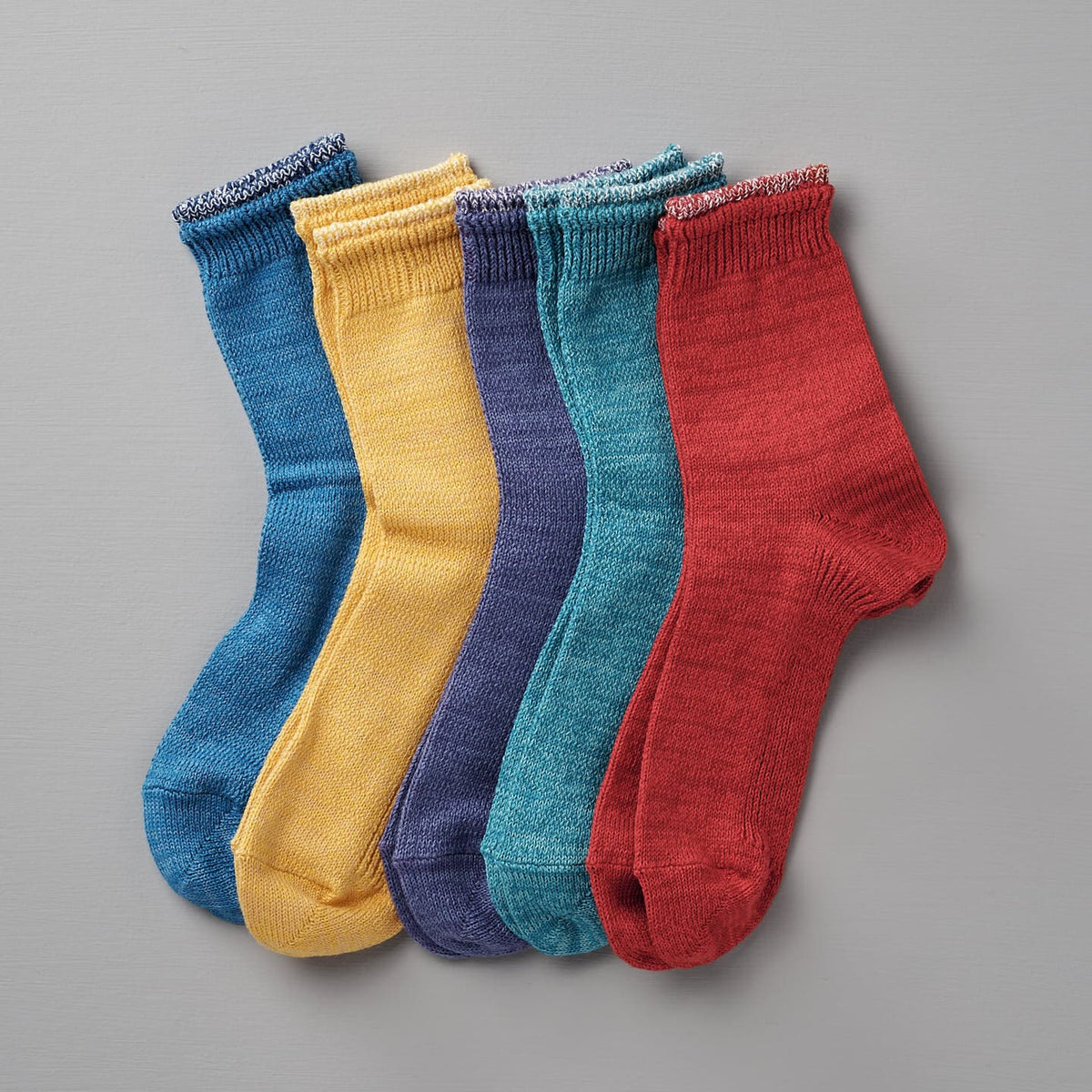 Five pairs of Mauna Kea Organic Top Switching Socks – Aqua, ranging in sizes EUR 35—38 and EUR 39—42, are laid out in a row on a gray background. The vibrant colors of the socks include blue, yellow, purple, teal, and red.