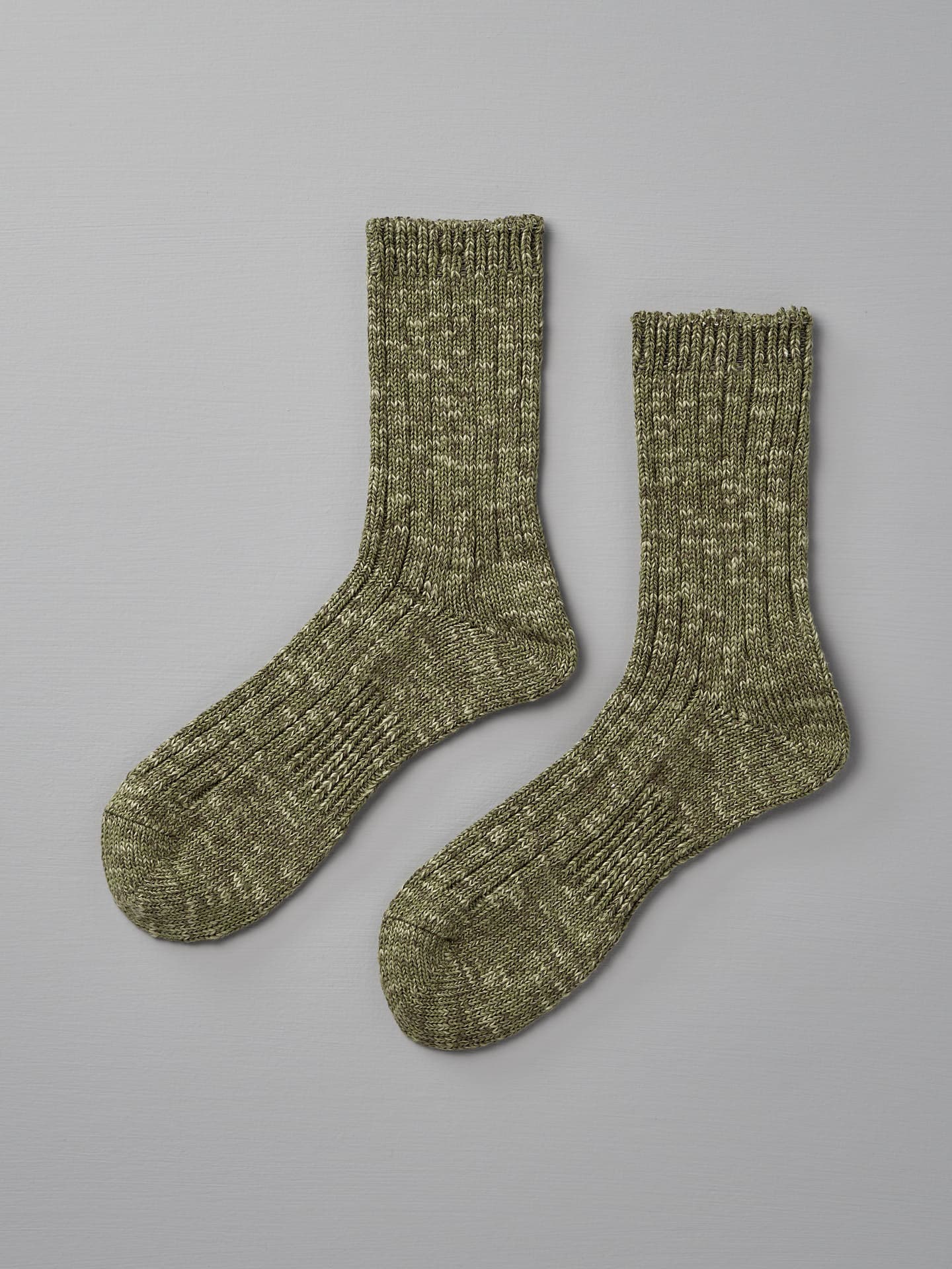 Two olive green, ribbed knit socks are displayed against a light gray background, fitting sizes EUR cm 23—25 and 35—38. The product is Japanese Slub Rib Socks – Green by Mauna Kea.