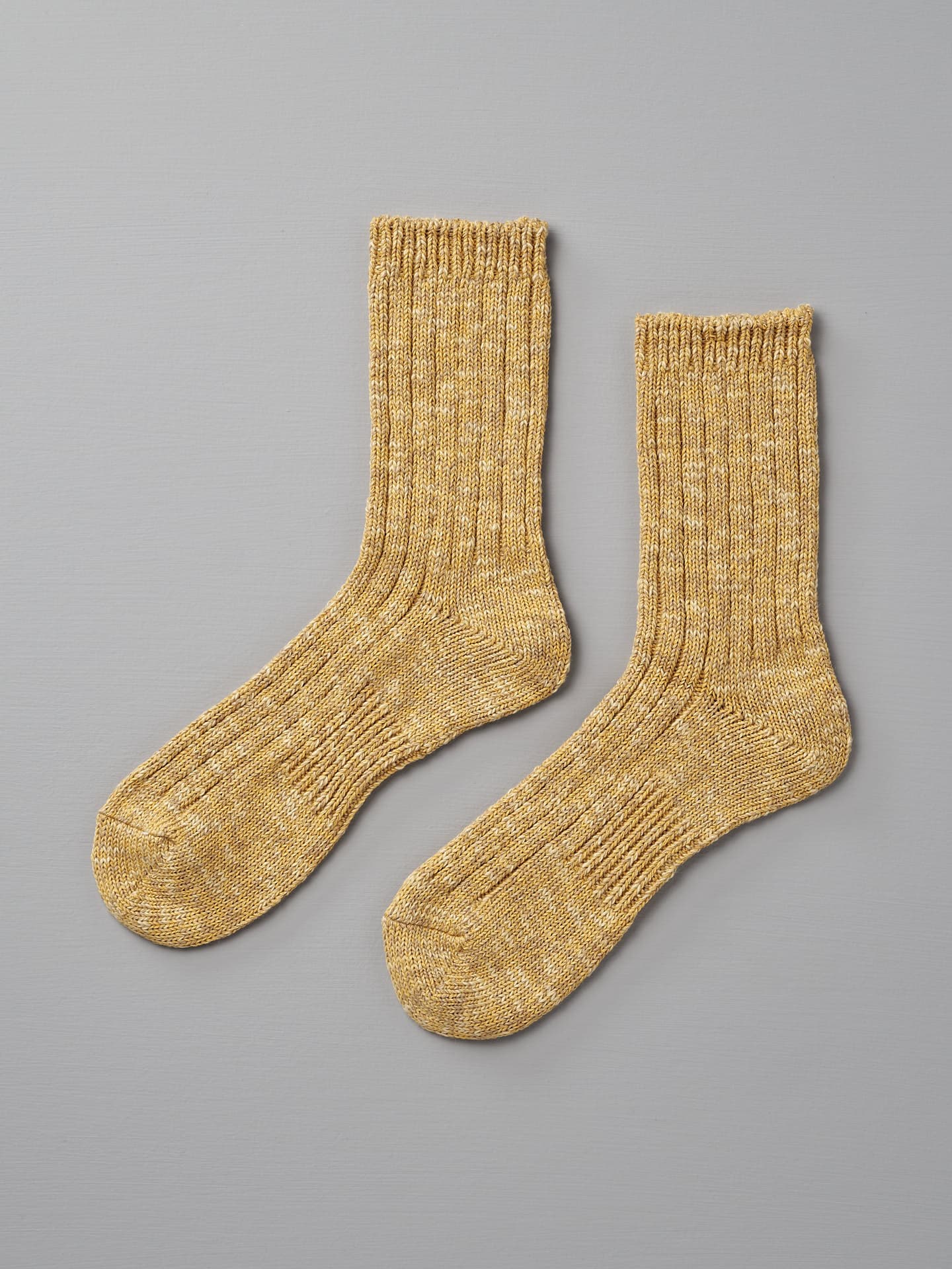 A pair of yellow knitted socks, fitting EUR 35—38, lies flat on a gray background. The Japanese Slub Rib Socks – Mustard by Mauna Kea have a ribbed texture extending from the cuffs to the toes.