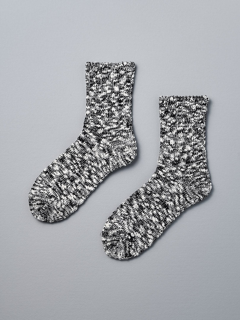 A pair of Mauna Kea Japanese Slub Socks – Black on a grey background, made from a cotton and hemp blend using vintage knitting machines.