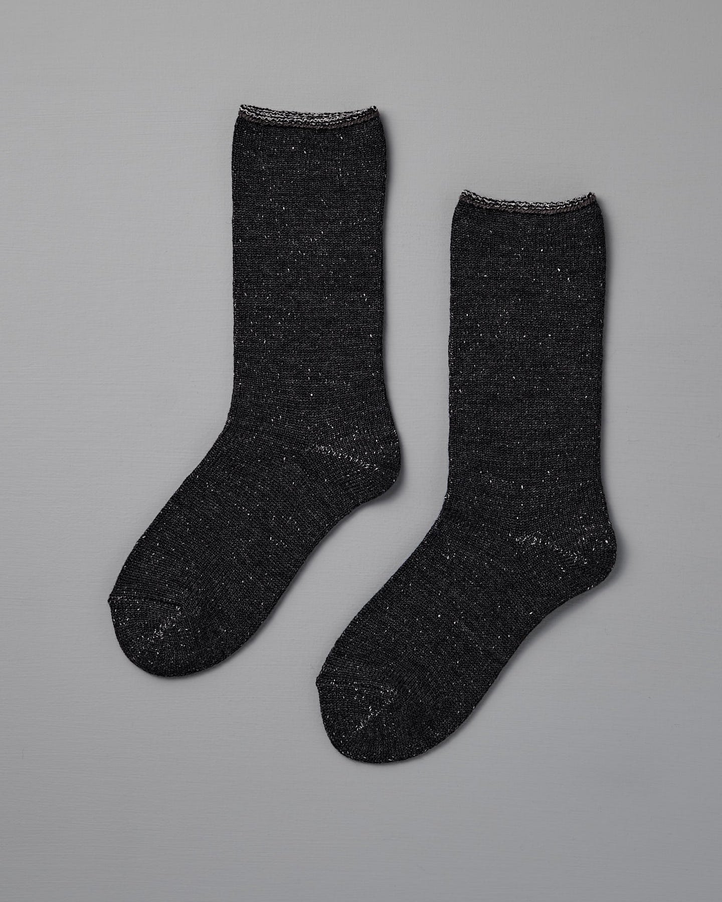 A pair of Nishiguchi Kutsushita Memeri Wool Silk Socks in charcoal, crew-length and made in Japan, laid flat on a plain grey background.