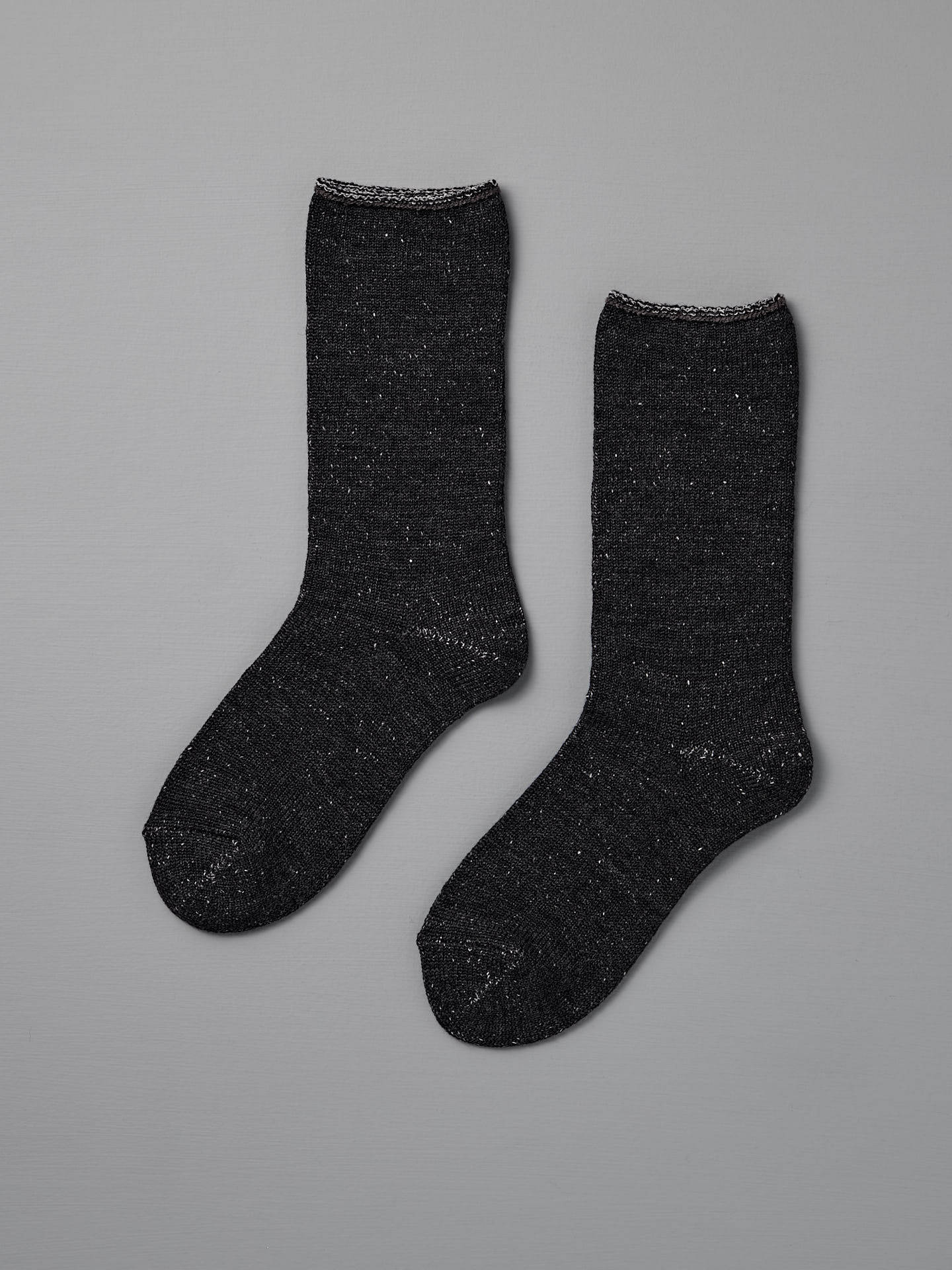 A pair of Nishiguchi Kutsushita Memeri Wool Silk Socks in charcoal, crew-length and made in Japan, laid flat on a plain grey background.