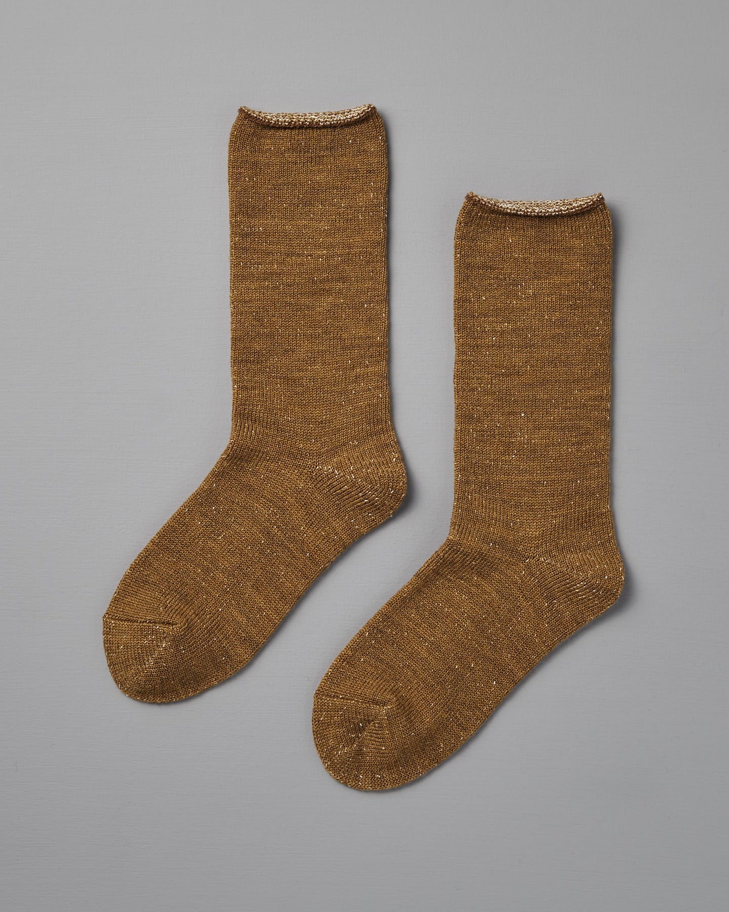 A pair of Memeri Wool Silk Socks in mustard by Nishiguchi Kutsushita, shown flat on a gray background. Made in Japan, these cozy socks blend warmth and style with a subtle sheen—perfect for any outfit.