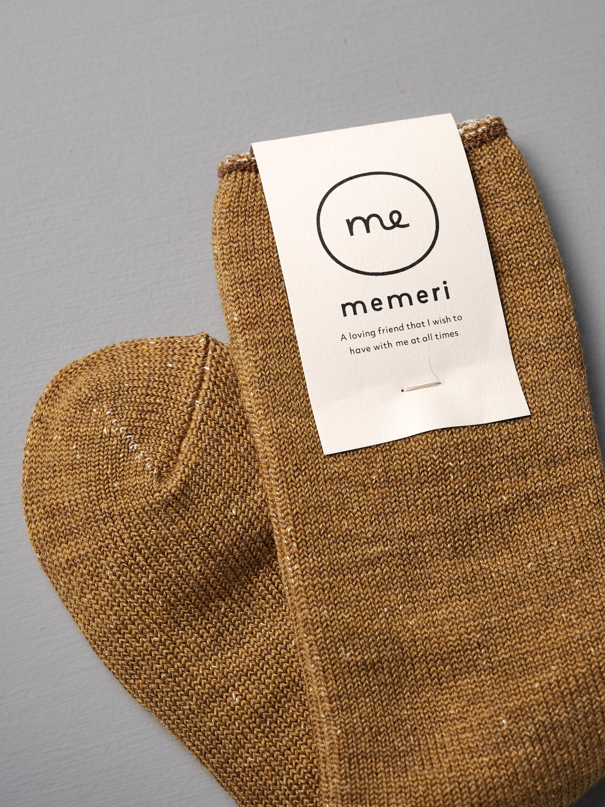 A pair of cozy mustard Memeri Wool Silk Socks by Nishiguchi Kutsushita, placed on a gray surface—exceptionally soft and luxurious for everyday comfort.