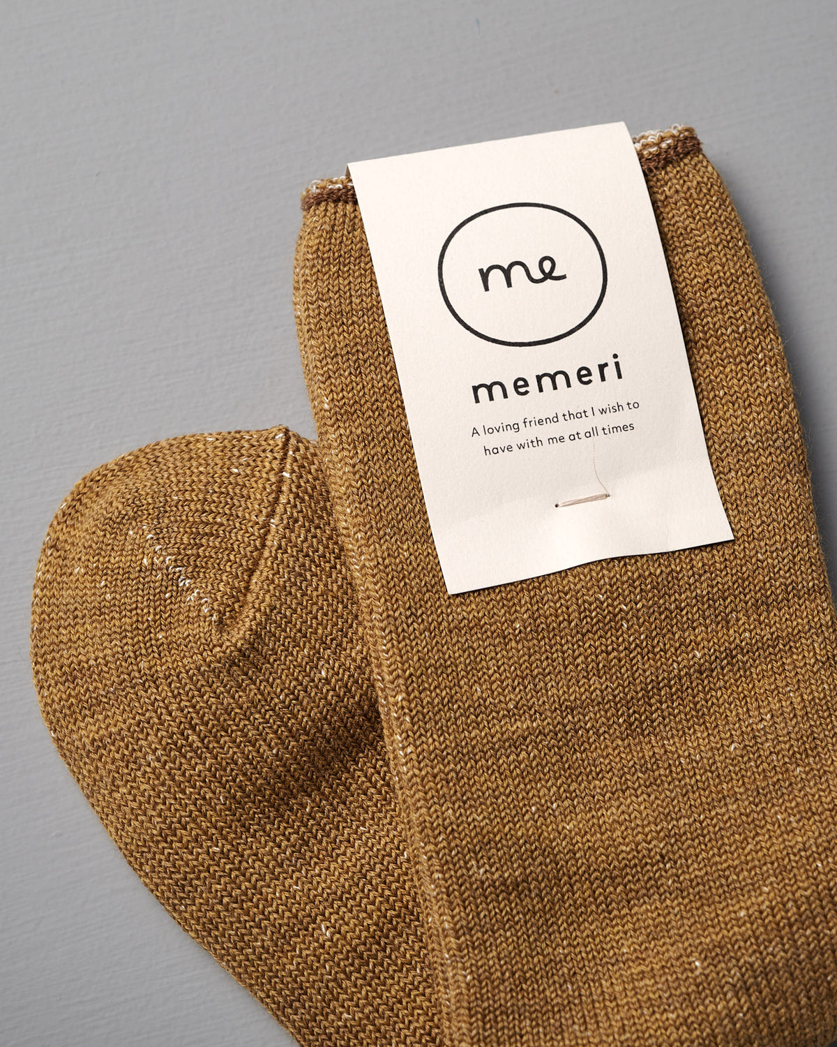 A pair of cozy mustard Memeri Wool Silk Socks by Nishiguchi Kutsushita, placed on a gray surface—exceptionally soft and luxurious for everyday comfort.