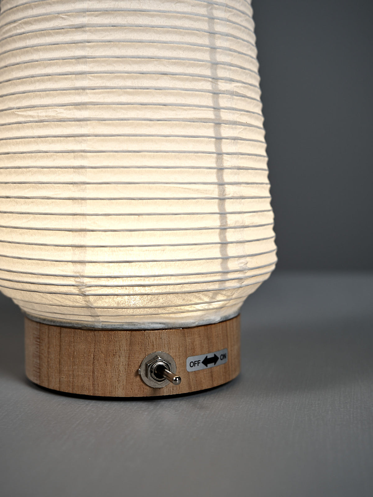 The Washi Paper LED Lantern – Itomaki features a ribbed white shade on a wooden base, with a metal toggle switch labeled "OFF" and "ON," showcasing the minimalist style of designer Rina Ono.