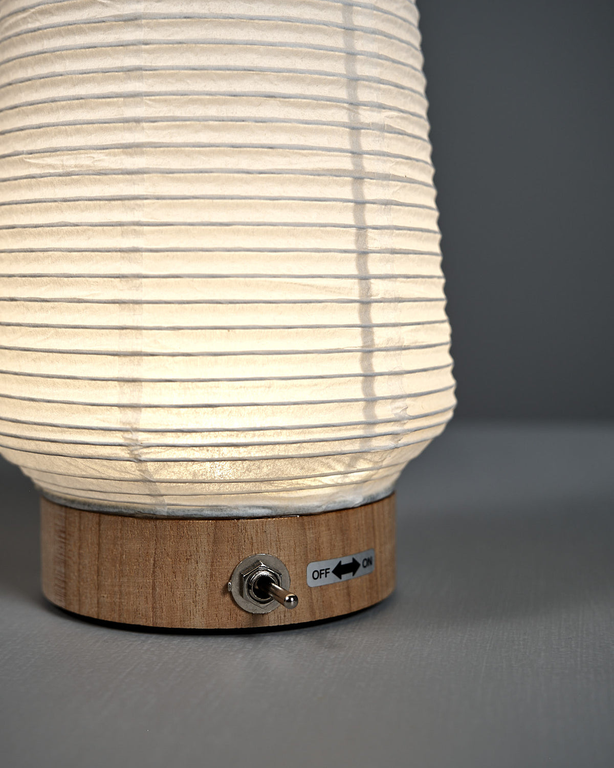The Washi Paper LED Lantern – Itomaki features a ribbed white shade on a wooden base, with a metal toggle switch labeled "OFF" and "ON," showcasing the minimalist style of designer Rina Ono.
