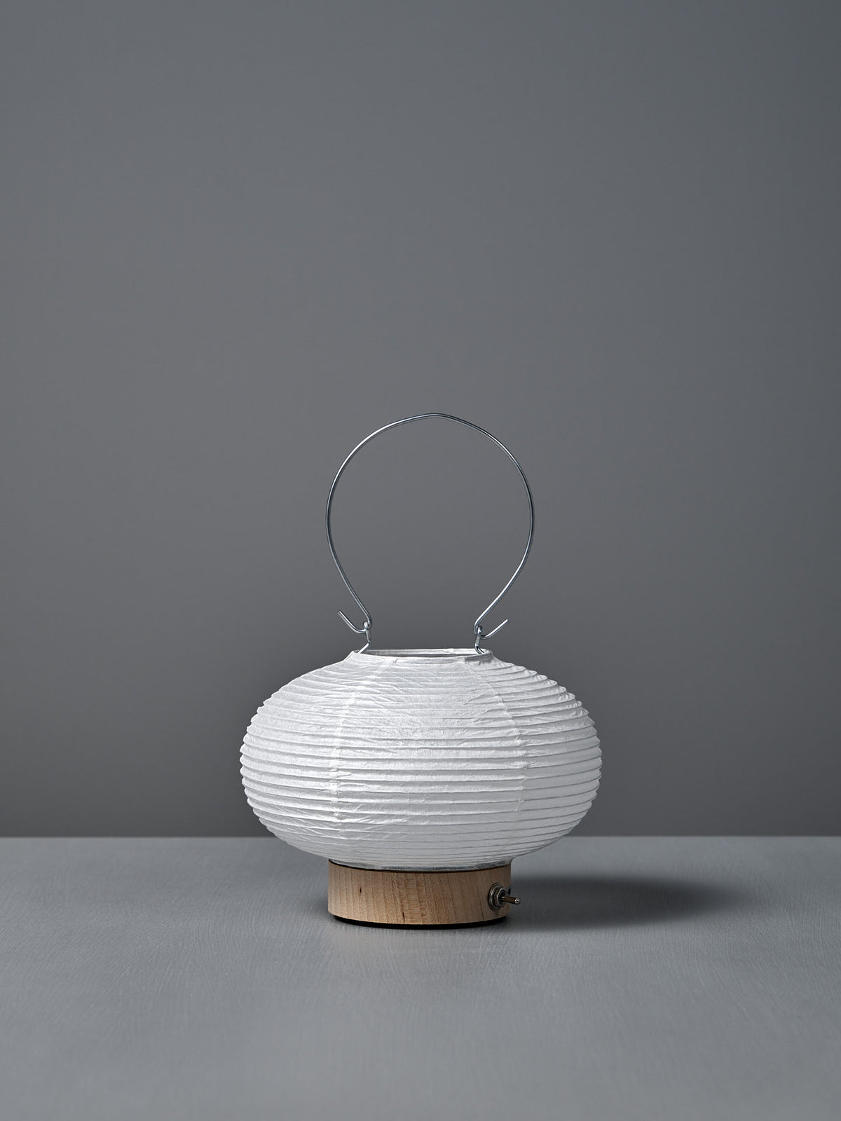 The Washi Paper LED Lantern – Maru, designed by Rina Ono, is a small, round white lantern with a metal handle and a light wooden base, displayed against a plain gray background.