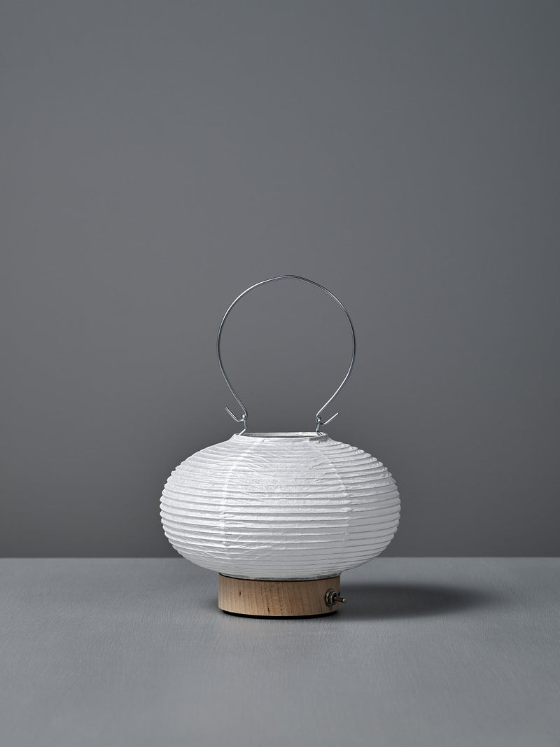 The Washi Paper LED Lantern – Maru, designed by Rina Ono, is a small, round white lantern with a metal handle and a light wooden base, displayed against a plain gray background.