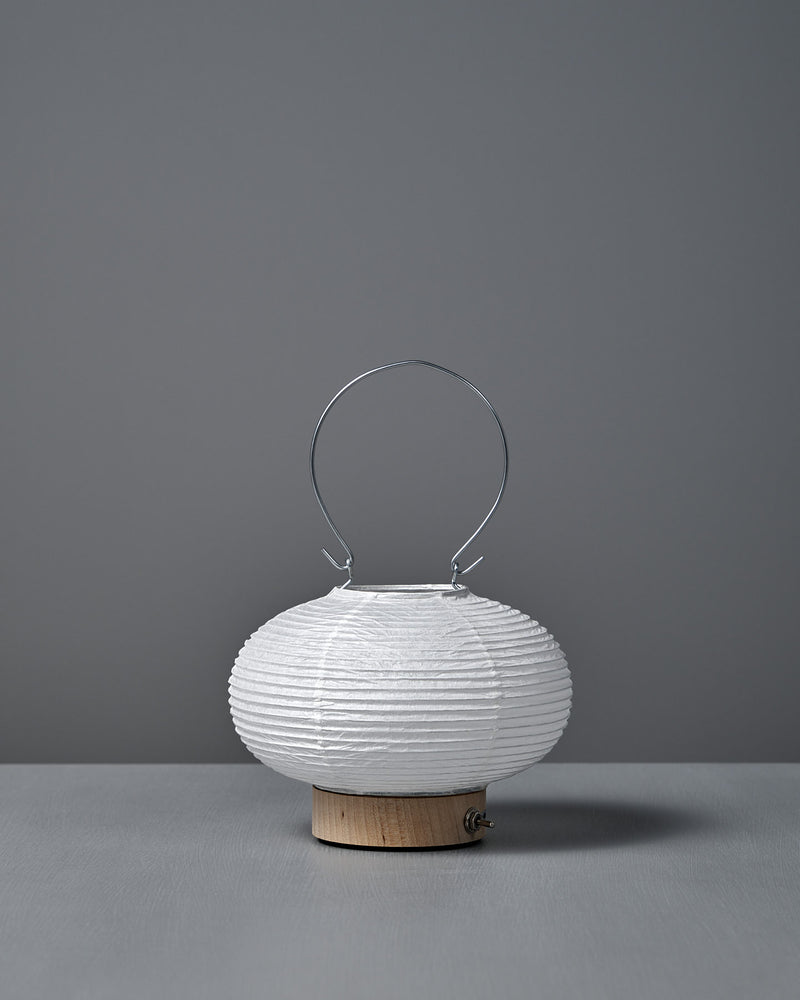 The Washi Paper LED Lantern – Maru, designed by Rina Ono, is a small, round white lantern with a metal handle and a light wooden base, displayed against a plain gray background.