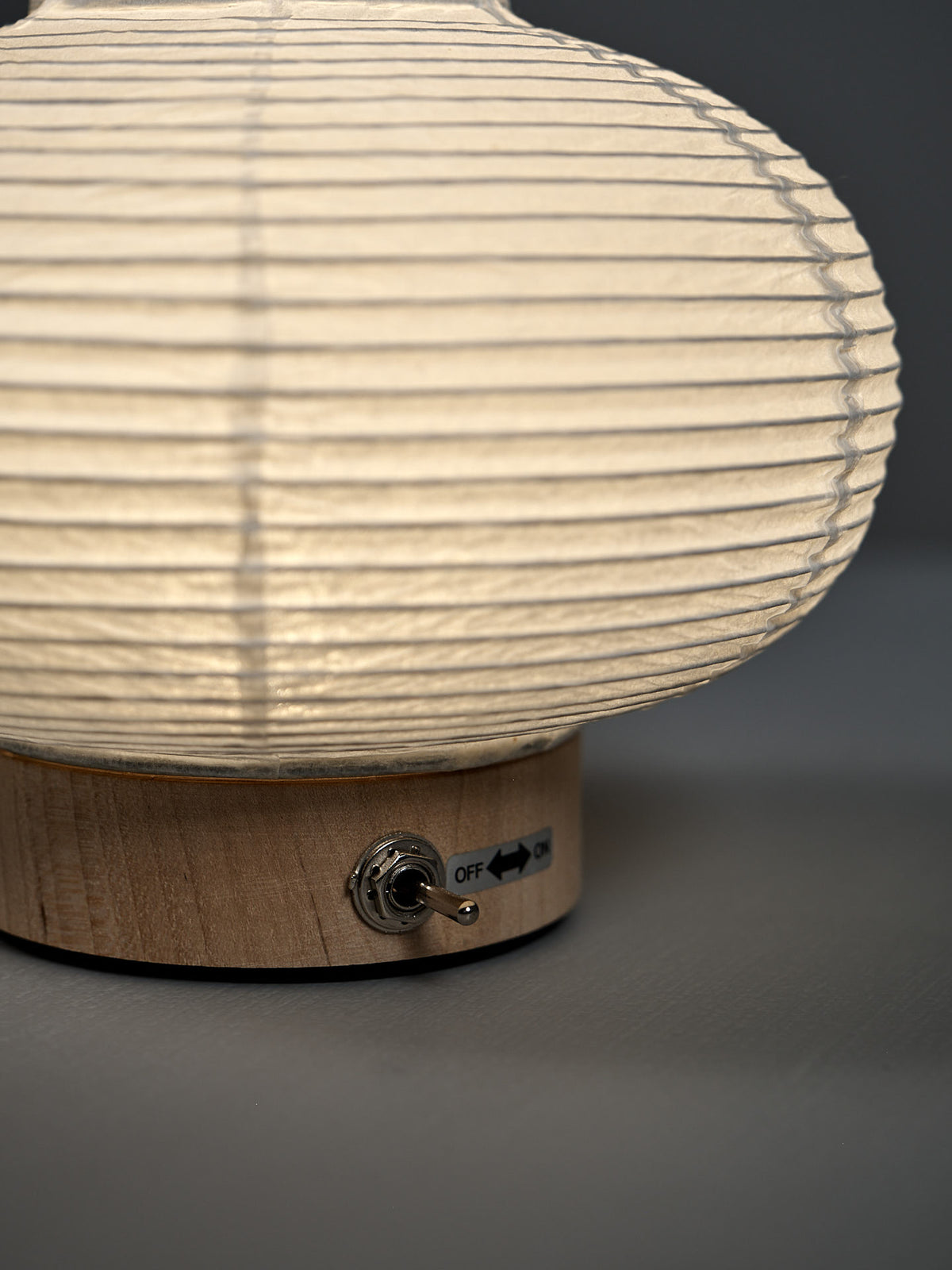 Close-up of the Washi Paper LED Lantern – Maru: a round paper lampshade on a wooden base with a metal toggle switch labeled "OFF" and "ON," crafted by Japanese designer Rina Ono.