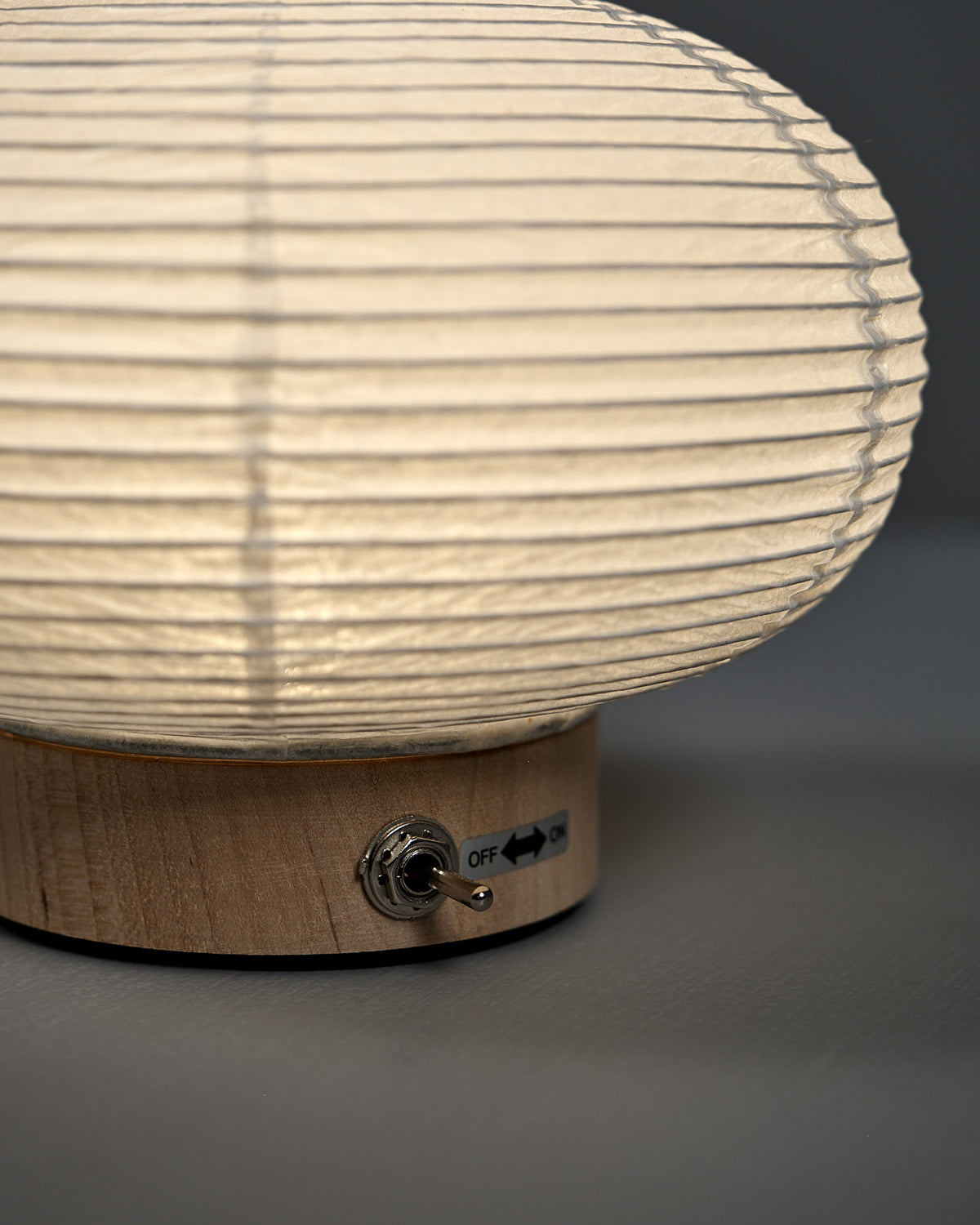Close-up of the Washi Paper LED Lantern – Maru: a round paper lampshade on a wooden base with a metal toggle switch labeled "OFF" and "ON," crafted by Japanese designer Rina Ono.