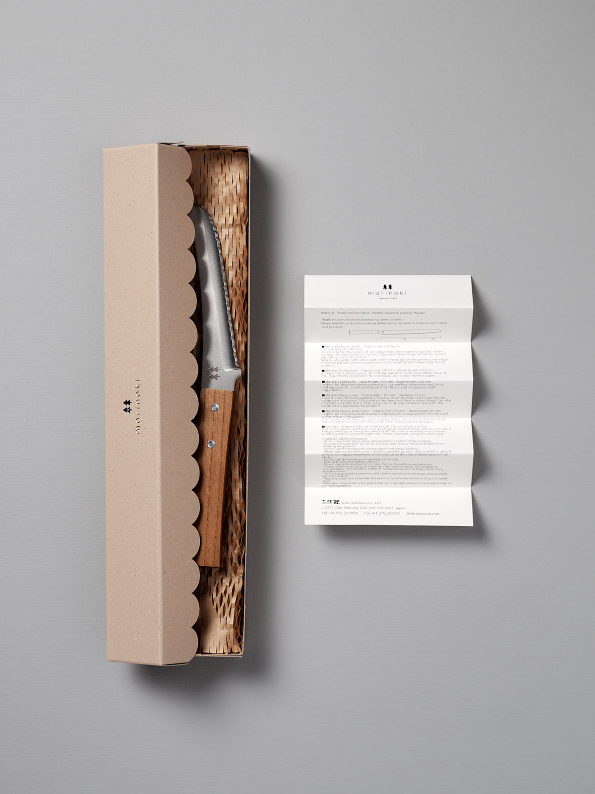 The Morinoki Soft Cheese Knife by Shizu Hamono Co. features a Japanese Zelkova wood handle and is presented in a cardboard box with textured packing and an instruction leaflet, highlighting exquisite Japanese craftsmanship.