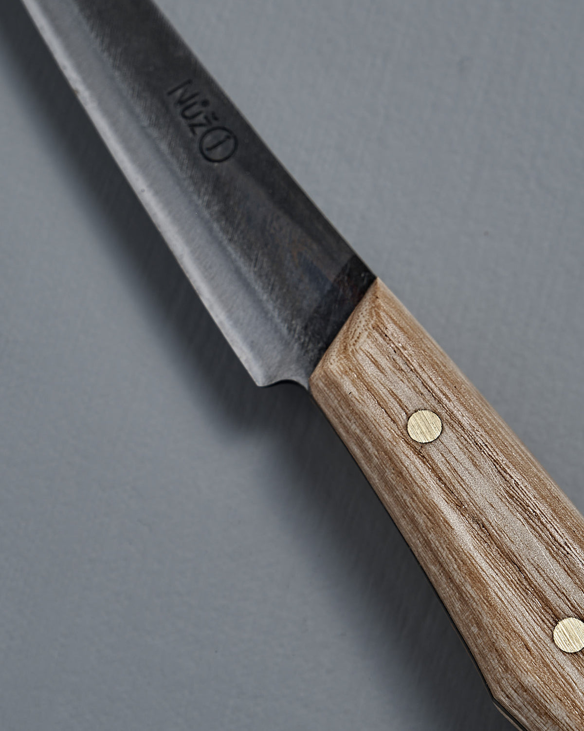 Close-up of the №1 – Spread Knife, featuring a handcrafted wooden handle and a dark Swedish carbon steel blade, resting on a gray textured surface.