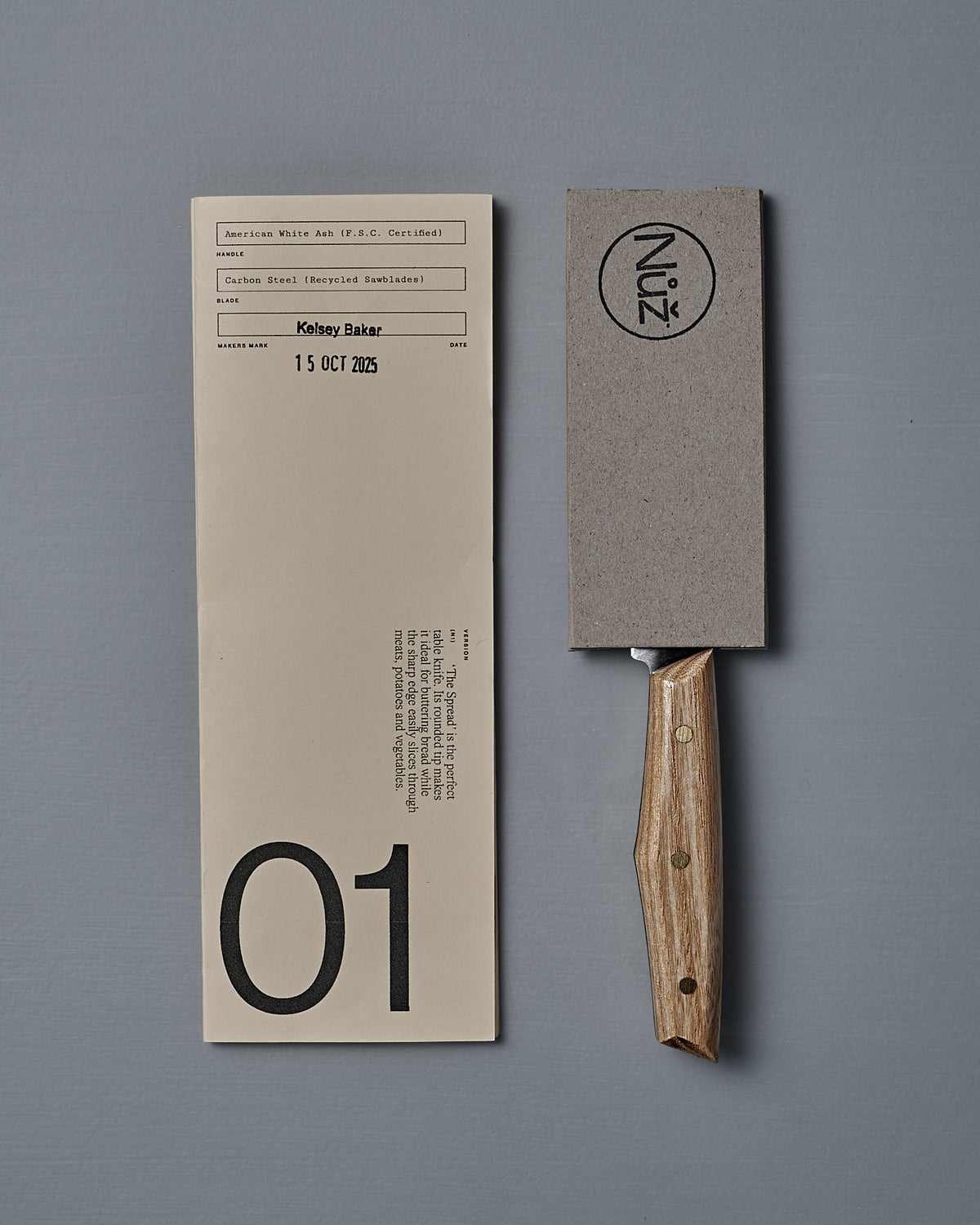 The №1 – Spread Knife, a handcrafted rectangular cleaver with a wooden handle, rests beside a document labeled "01" and dated "15 OCT 2023" on a gray background.