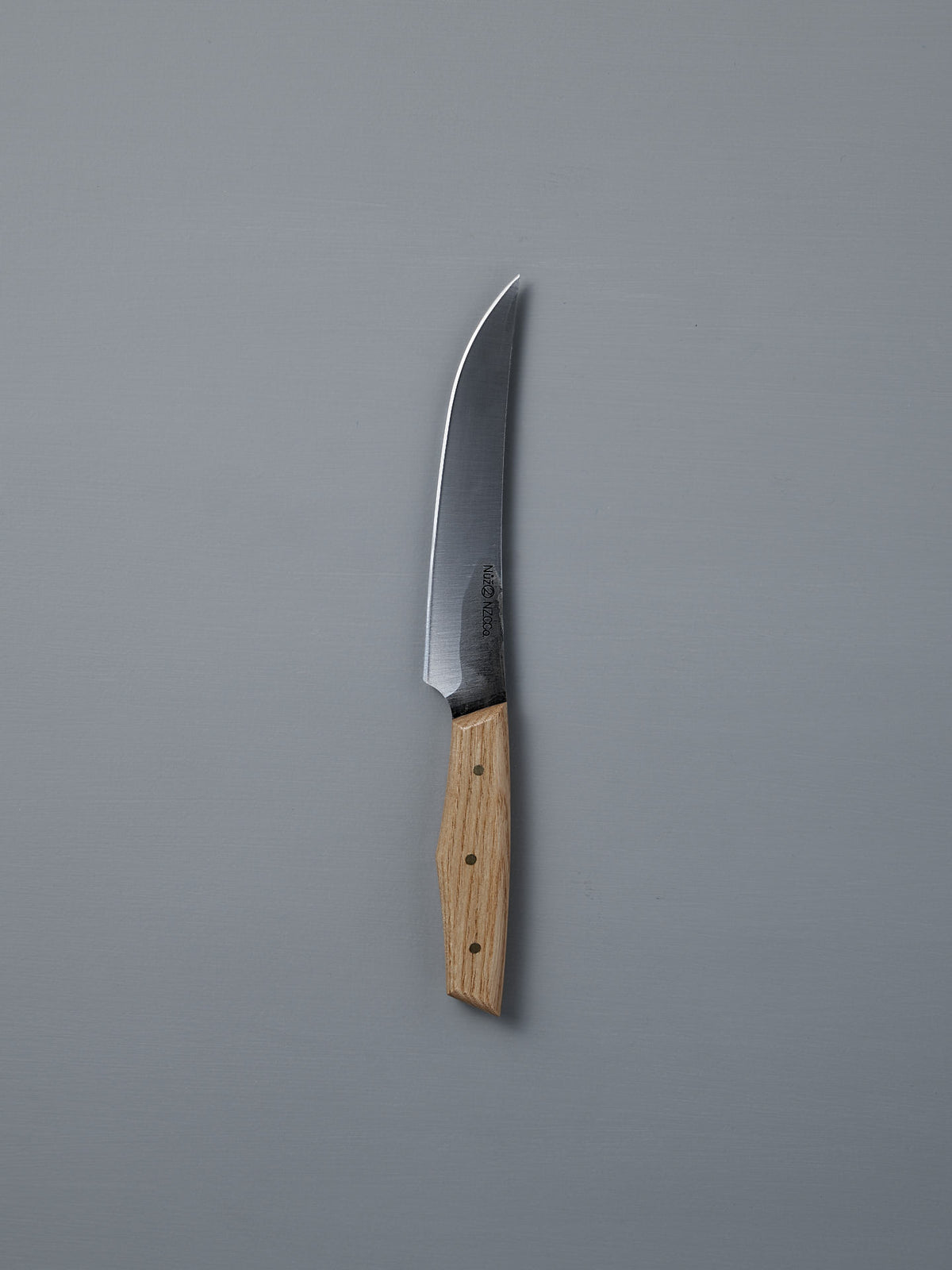 The №2 – Farmer Knife, featuring a handcrafted curved stainless steel blade and a light wood handle, rests on a plain gray surface—ideal as an everyday prep knife.