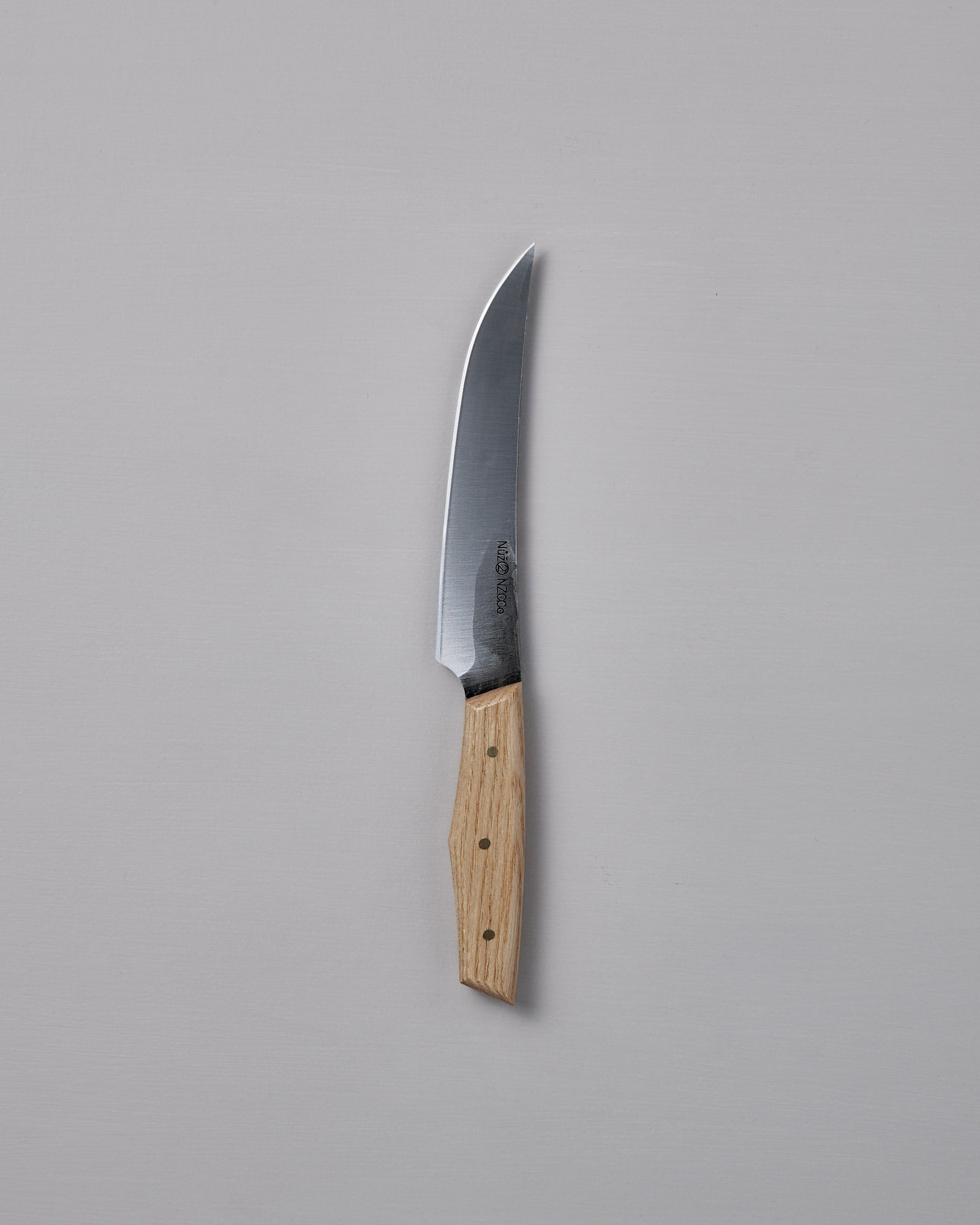 The №2 – Farmer Knife, featuring a handcrafted curved stainless steel blade and a light wood handle, rests on a plain gray surface—ideal as an everyday prep knife.