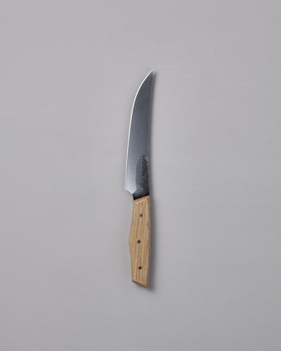 The №2 – Farmer Knife, featuring a handcrafted curved stainless steel blade and a light wood handle, rests on a plain gray surface—ideal as an everyday prep knife.