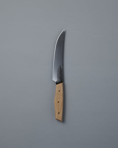 The №2 – Farmer Knife, featuring a handcrafted curved stainless steel blade and a light wood handle, rests on a plain gray surface—ideal as an everyday prep knife.