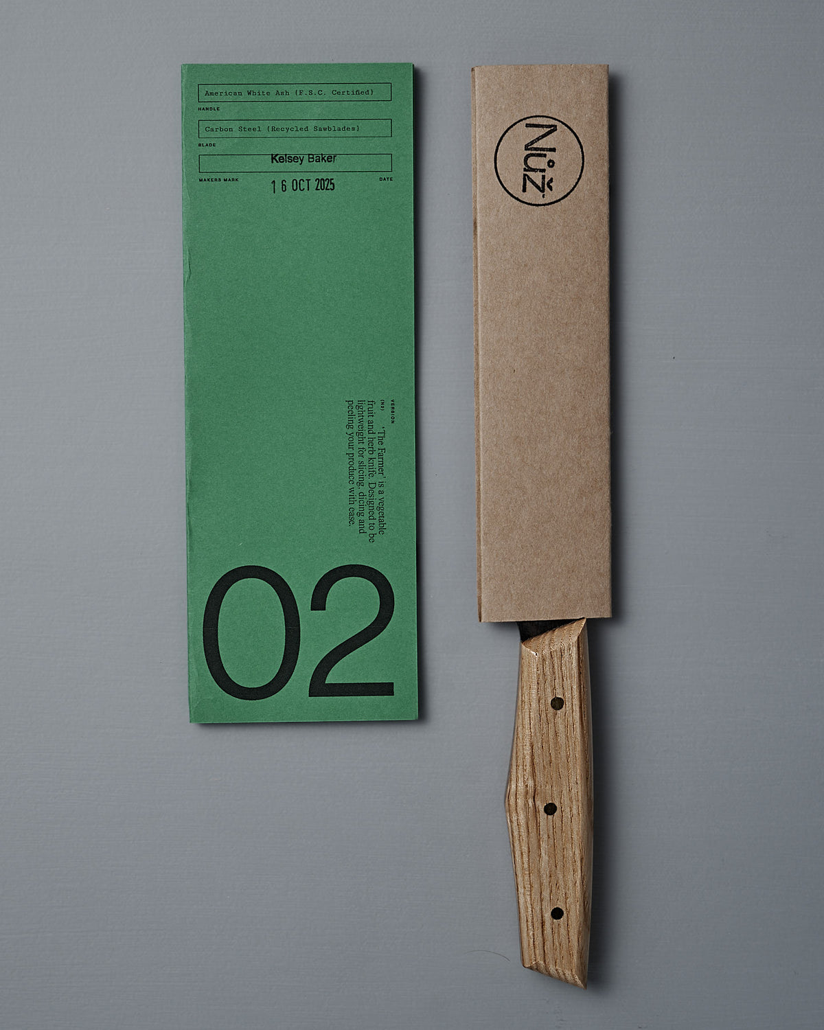 A green paper form labeled "02" sits beside the №2 – Farmer Knife with an American Ash handle, partly sheathed in brown cardboard bearing "Núz" branding, all arranged on a gray surface.