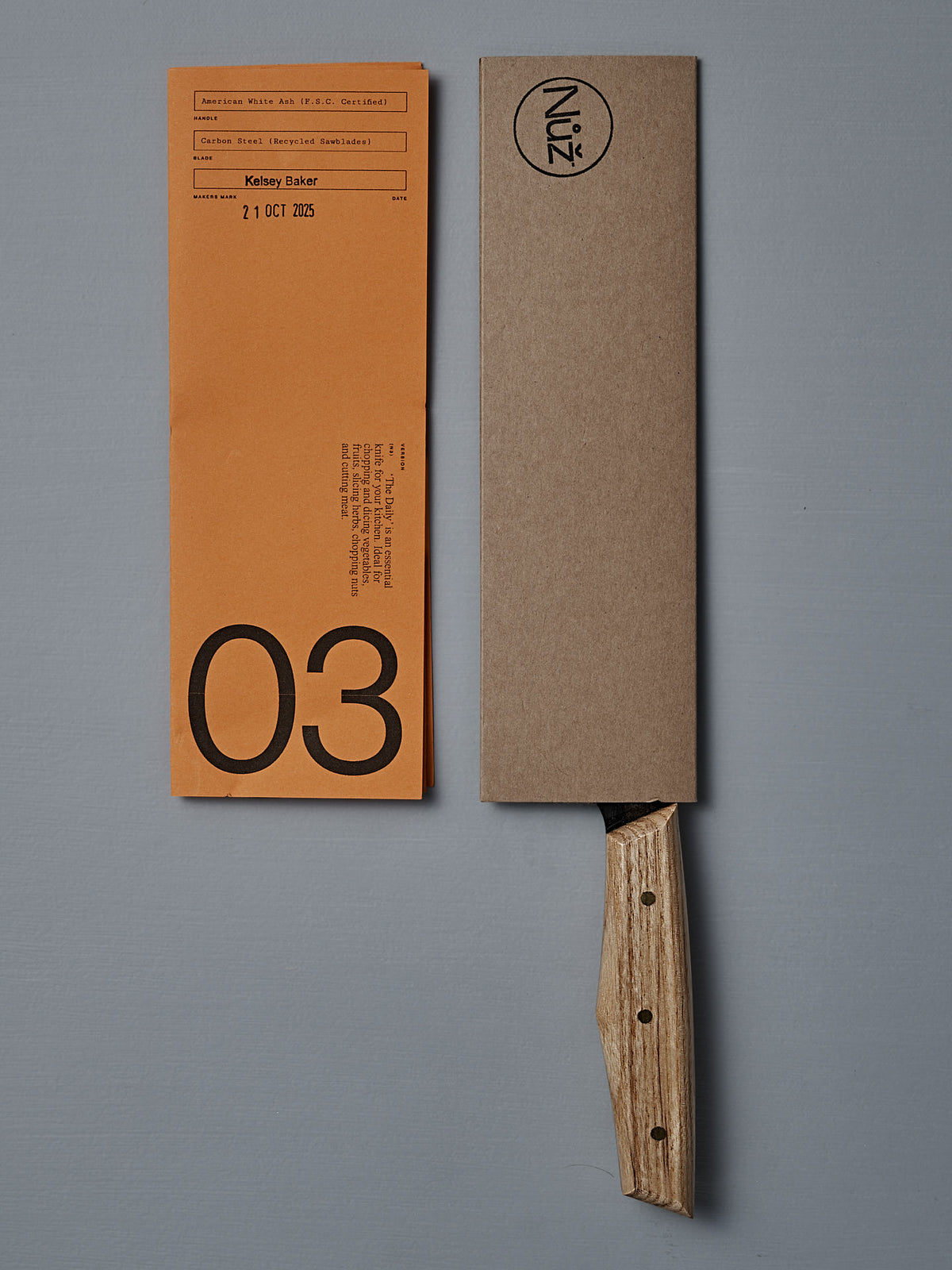 The №3 – Daily Knife, featuring a handcrafted American Ash handle and a brown cardboard sheath, rests next to an orange paper marked "03" and "21 OCT 2025.