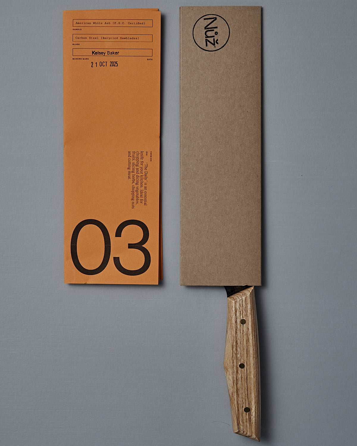 The №3 – Daily Knife, featuring a handcrafted American Ash handle and a brown cardboard sheath, rests next to an orange paper marked "03" and "21 OCT 2025.