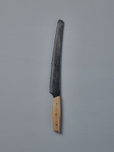 The №4 – Baker Knife, featuring a handcrafted serrated Swedish carbon steel blade and wooden handle, is displayed on a plain gray background.
