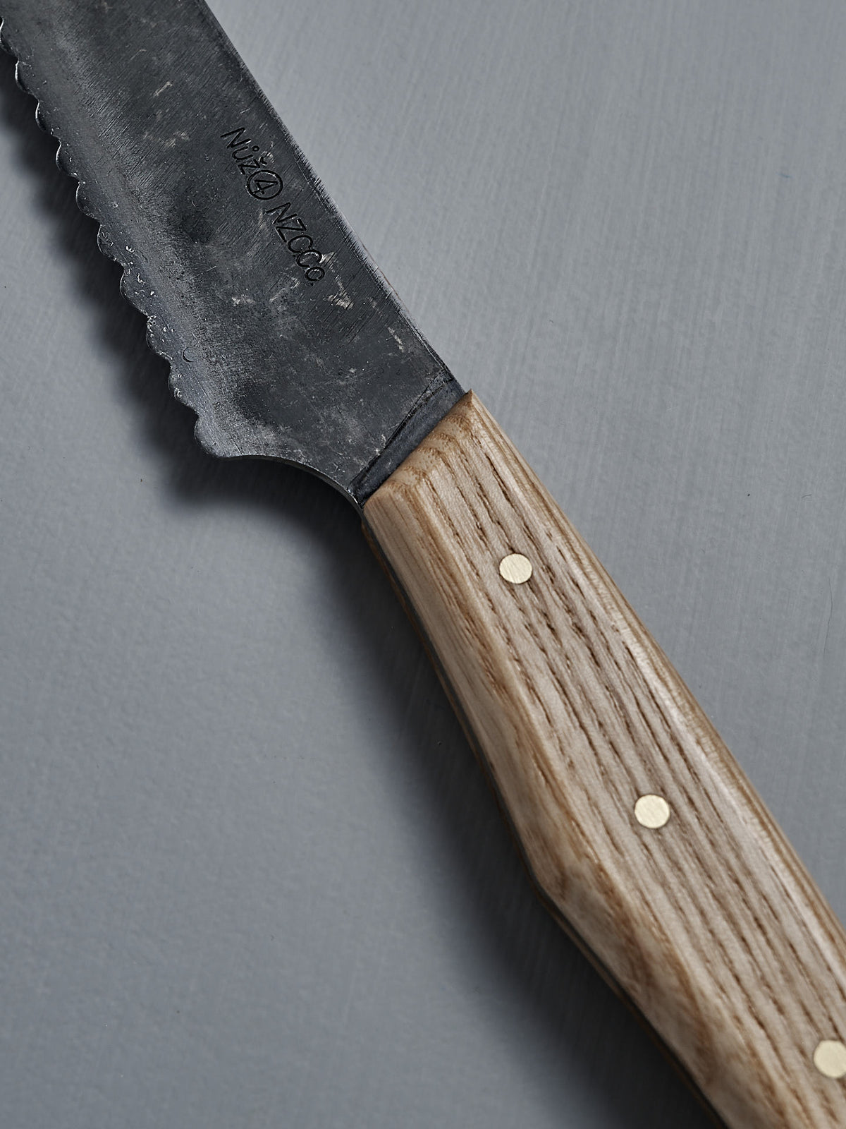 The №4 – Baker Knife, a handcrafted New Zealand bread knife with a carbon steel blade and wooden handle, rests on a gray surface.