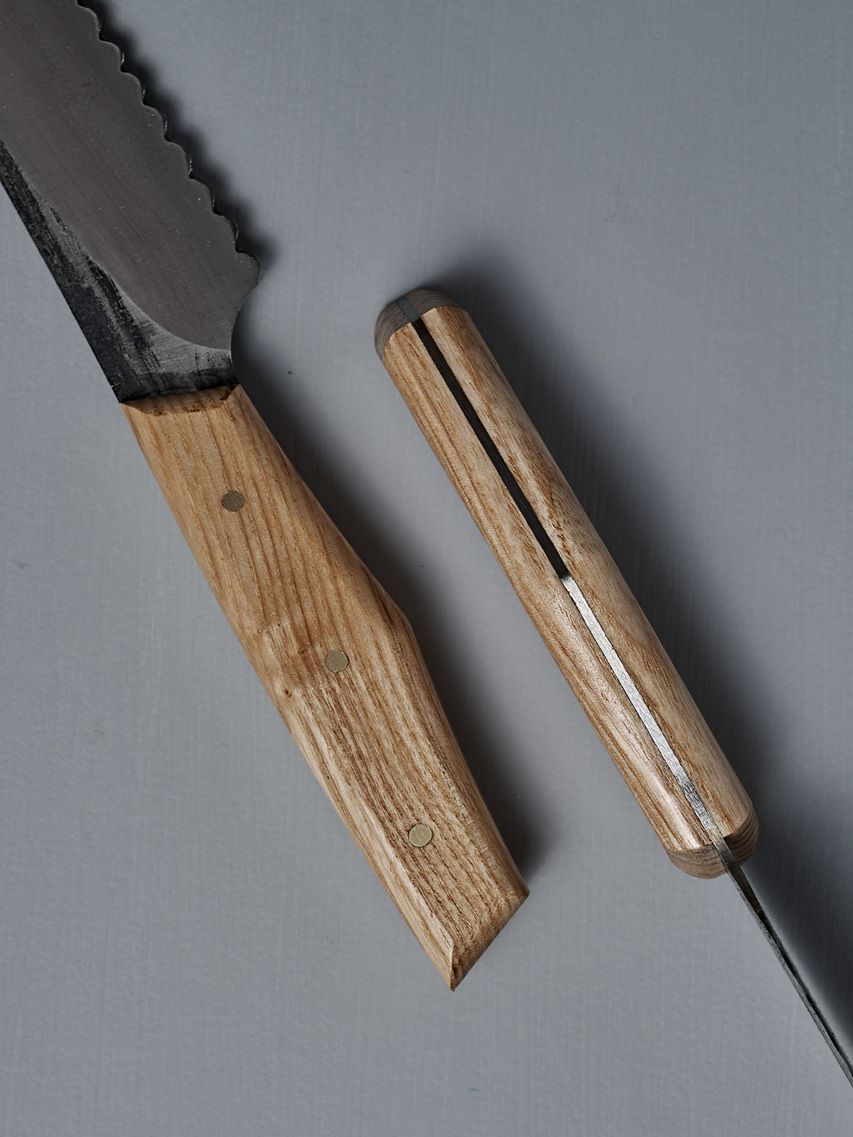 A close-up of the №4 – Baker Knife, showcasing a carbon steel blade and a wooden handle with metal rivets, placed on a gray surface.