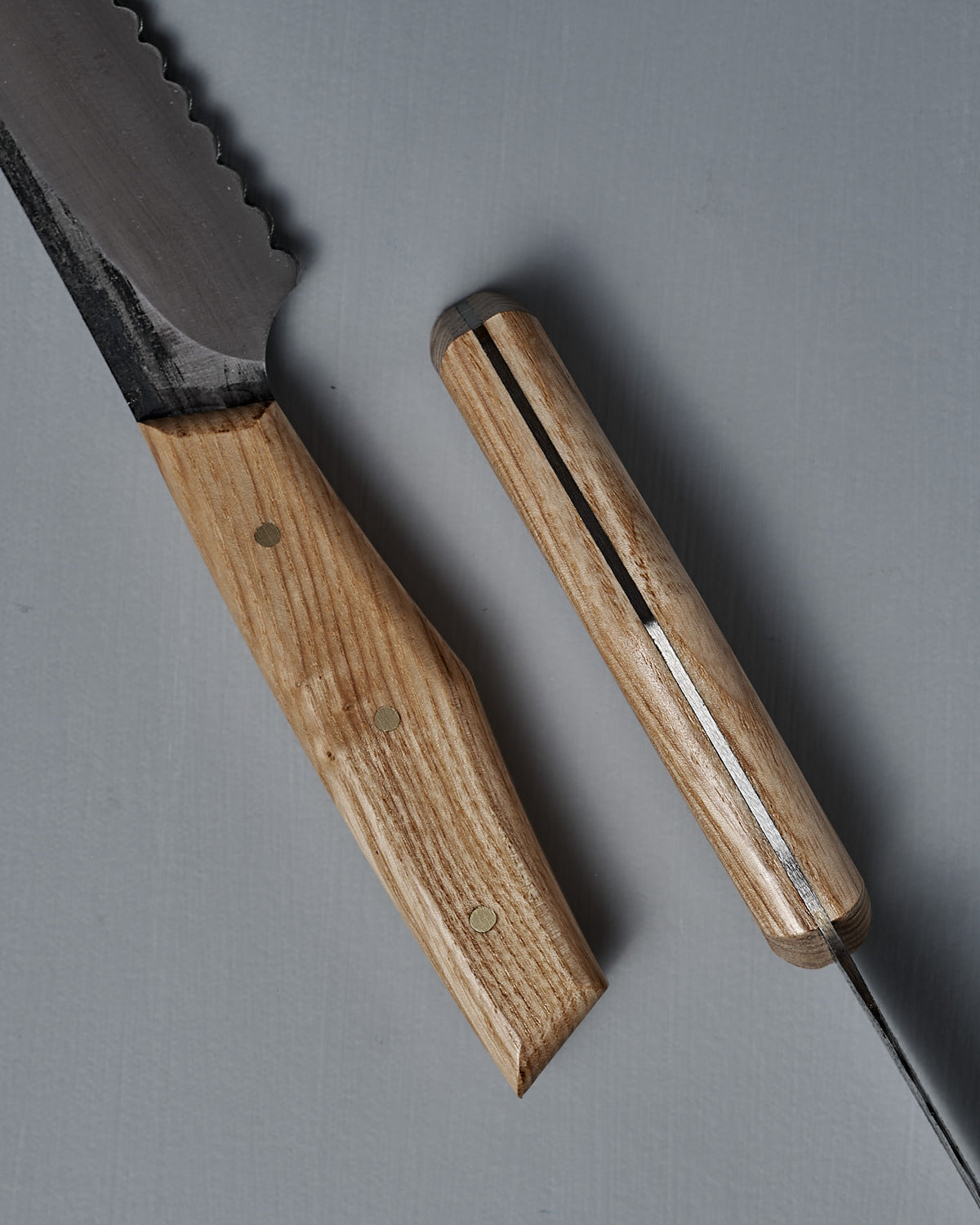 A close-up of the №4 – Baker Knife, showcasing a carbon steel blade and a wooden handle with metal rivets, placed on a gray surface.
