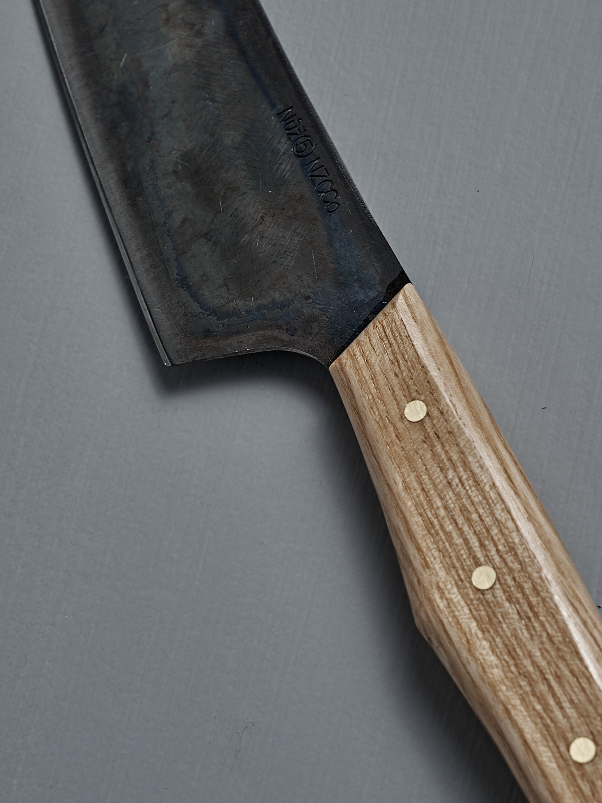 A close-up of the №5 – Gourmet Knife, handcrafted with a wooden handle, three brass rivets, and Swedish carbon steel blade, resting on a gray surface.