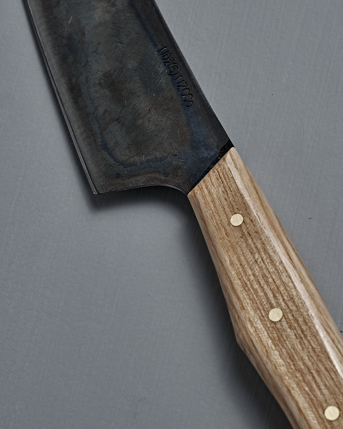 A close-up of the №5 – Gourmet Knife, handcrafted with a wooden handle, three brass rivets, and Swedish carbon steel blade, resting on a gray surface.